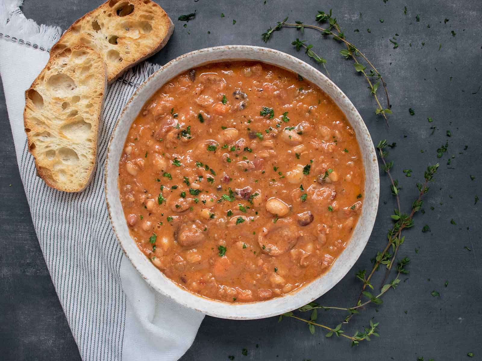 Overhead view of 15 Bean Soup in a light gray bowl with a side of sliced, toasted bread.