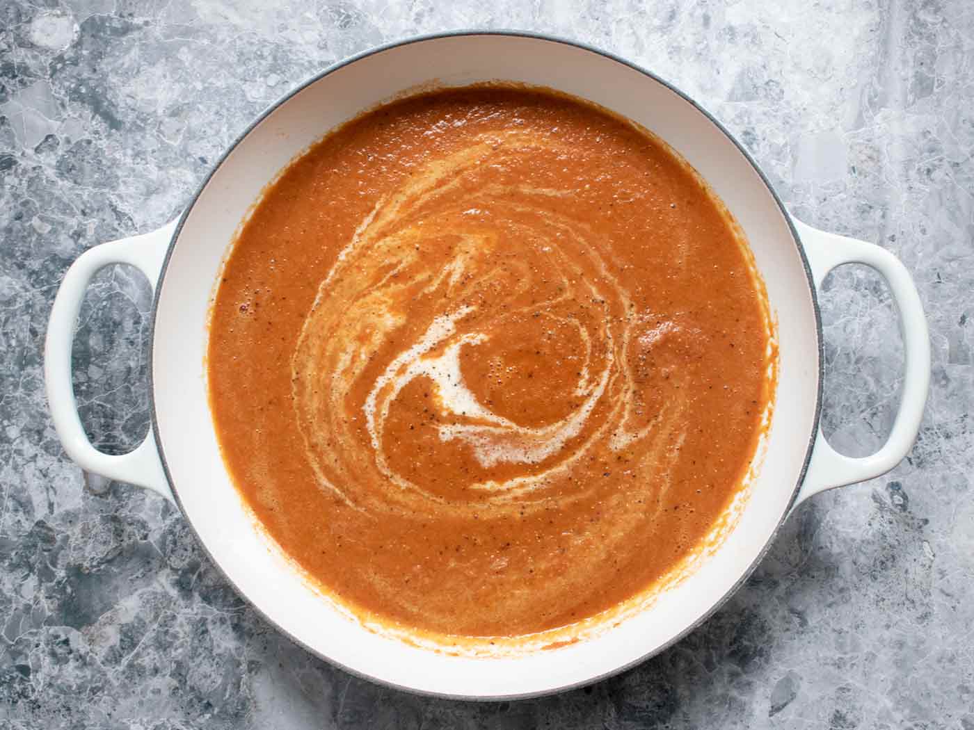 Overhead view of the finished soup in the pot, swirled with heavy cream.