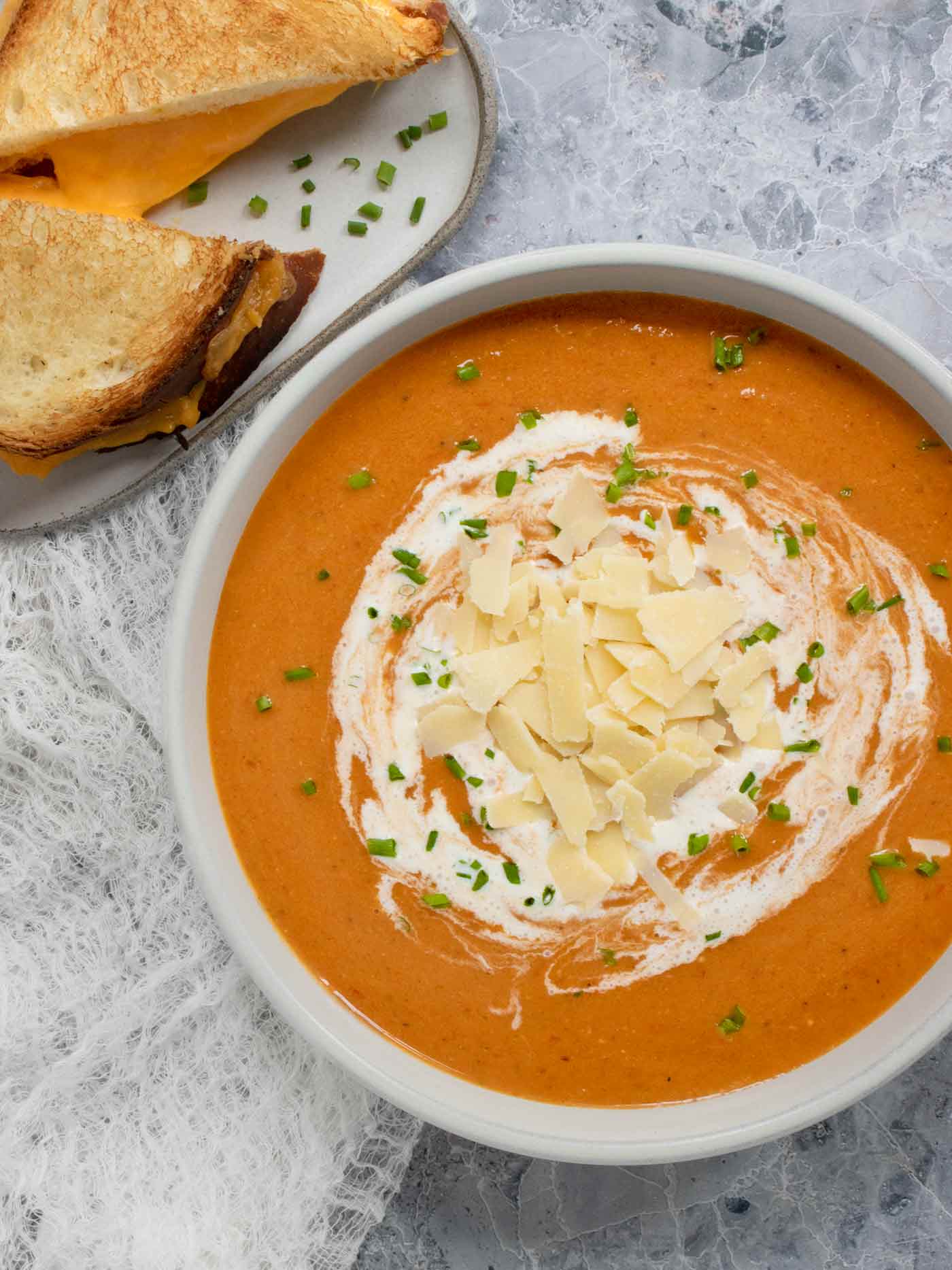 Overhead view of a bowl of Air Fryer Roasted Tomato Soup topped with shaved parmesan cheese, with a grilled cheese sandwich the side.