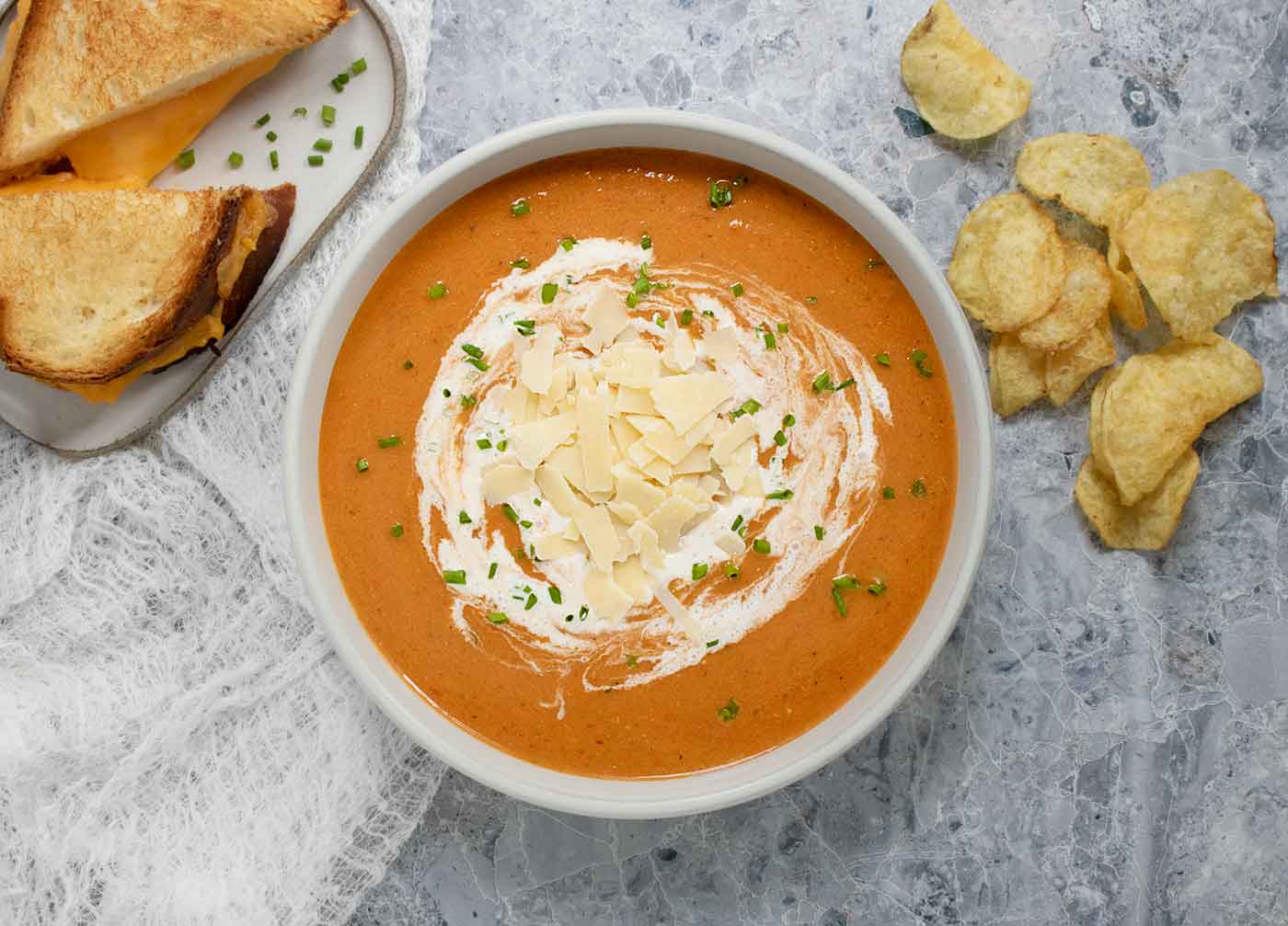 Overhead view of a bowl of Air Fryer Roasted Tomato Soup with a grilled cheese sandwich and potato chips on the side.