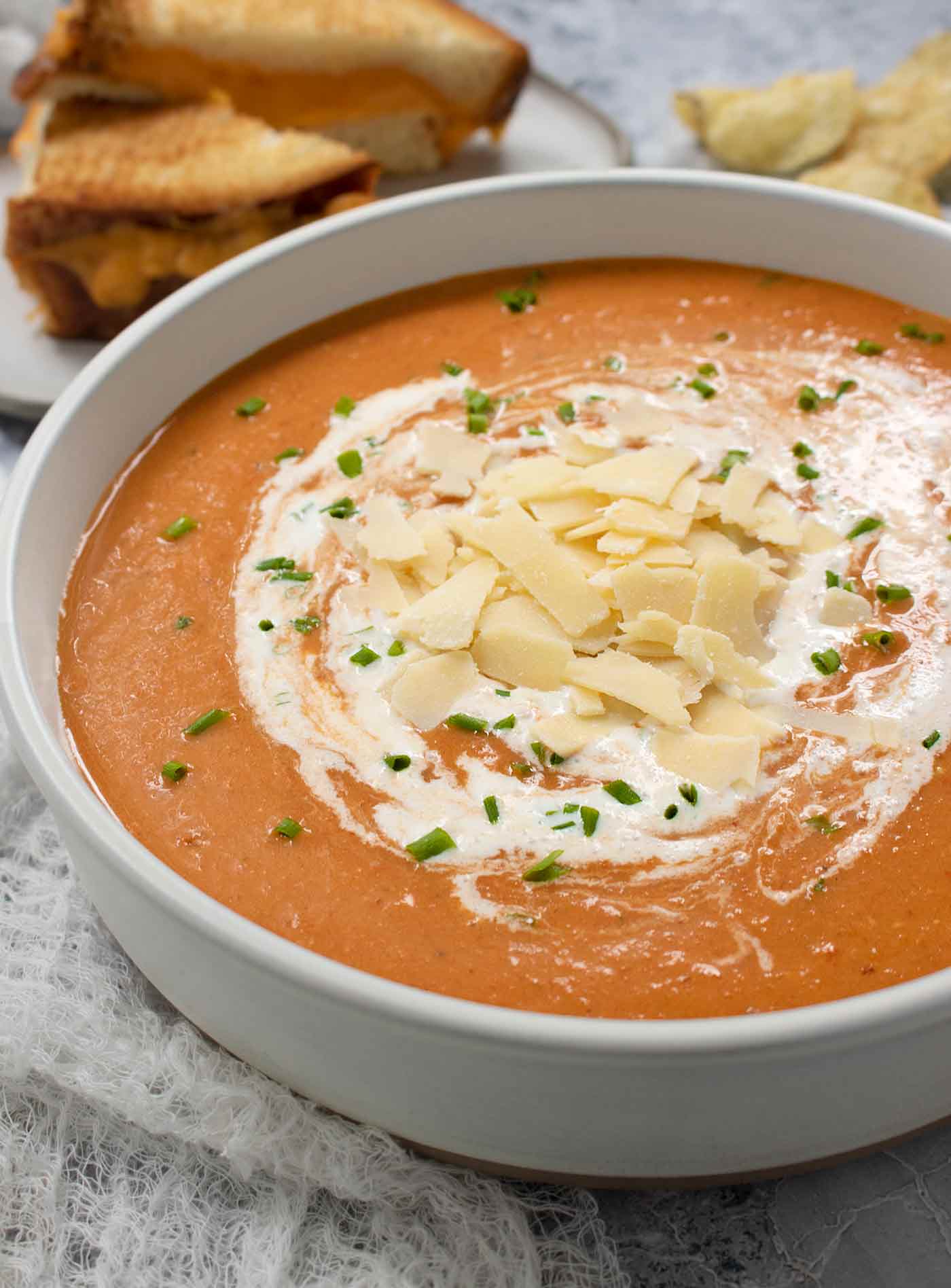 Side-angled view of a bowl of Air Fryer Roasted Tomato Soup with a grilled cheese sandwich in the background.