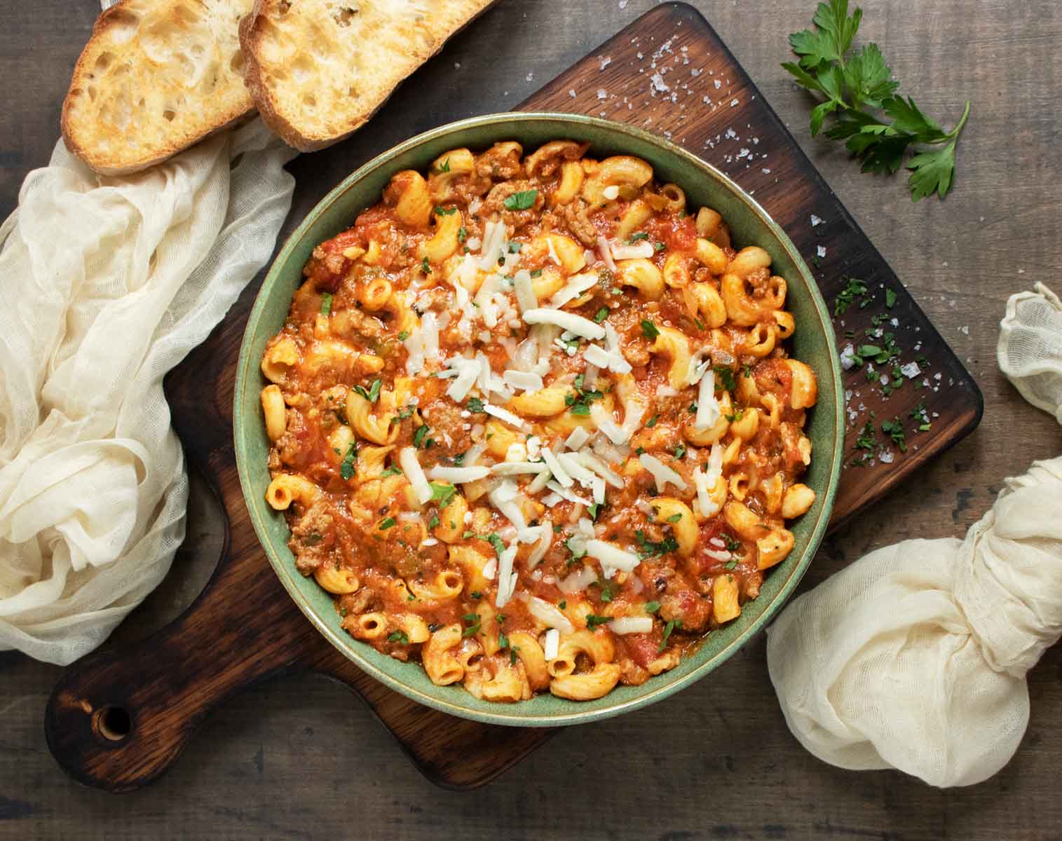American Goulash in a green serving bowl on a wooden board.