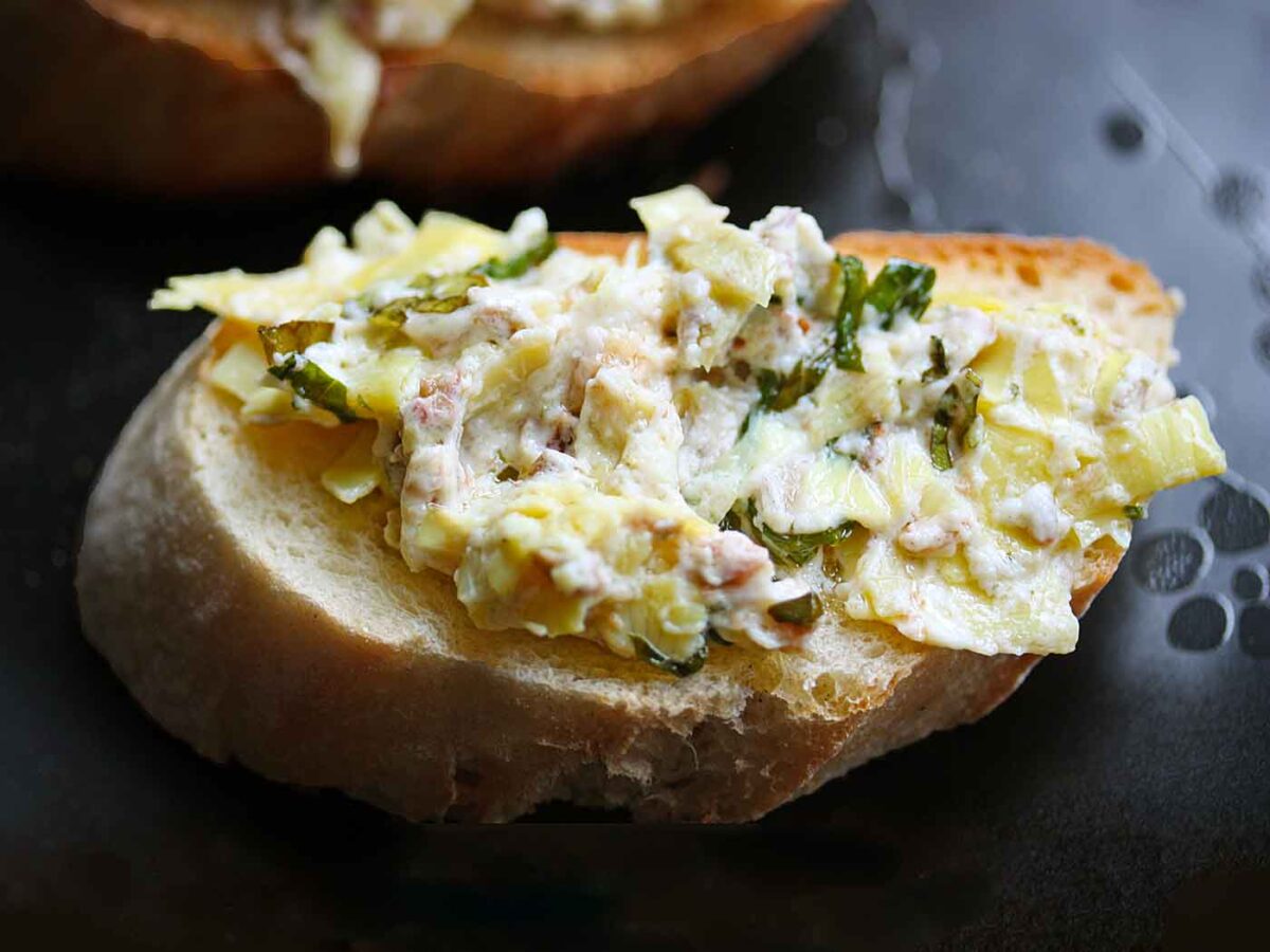 Baked Artichoke Olive Dip on a baguette slice.