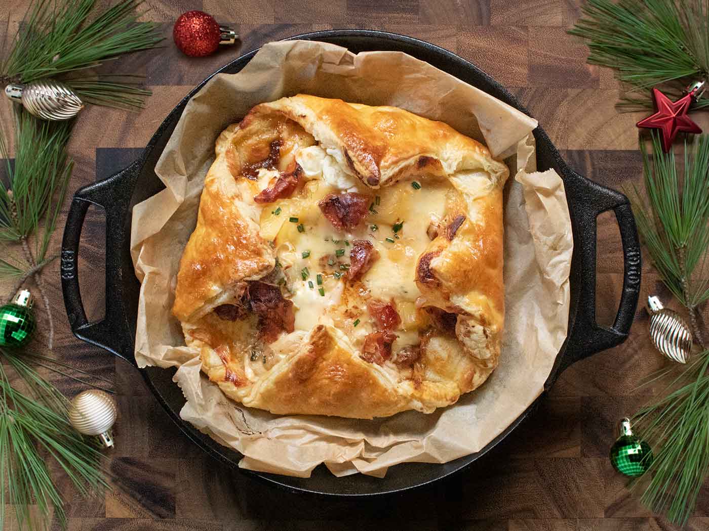 Baked Cheesy Puff Pastry with Crispy Prosciutto in a cast iron skillet, with holiday decorations on a serving board.