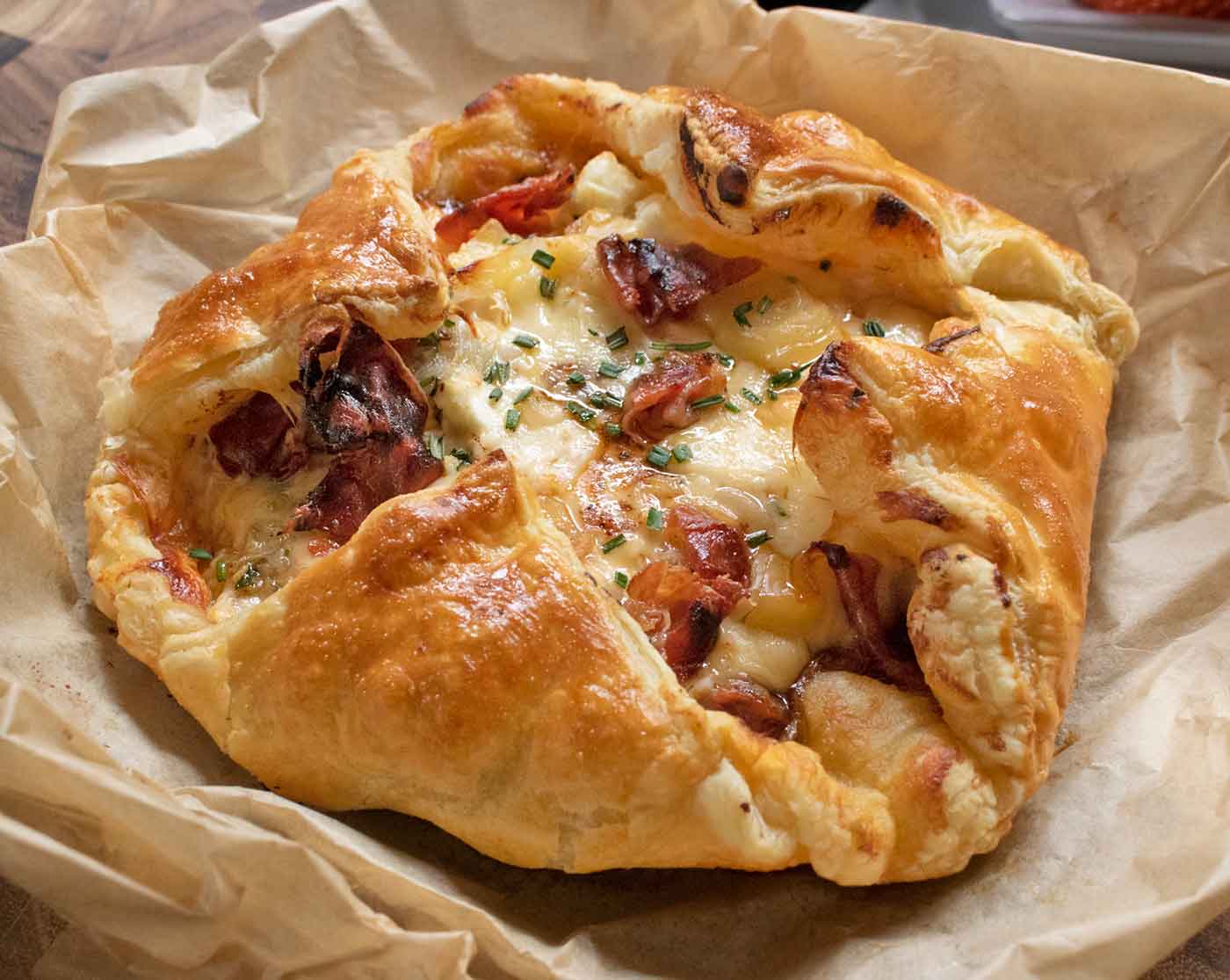 Side-angled view of Baked Cheesy Puff Pastry with Crispy Prosciutto, nestled in a sheet of parchment paper.
