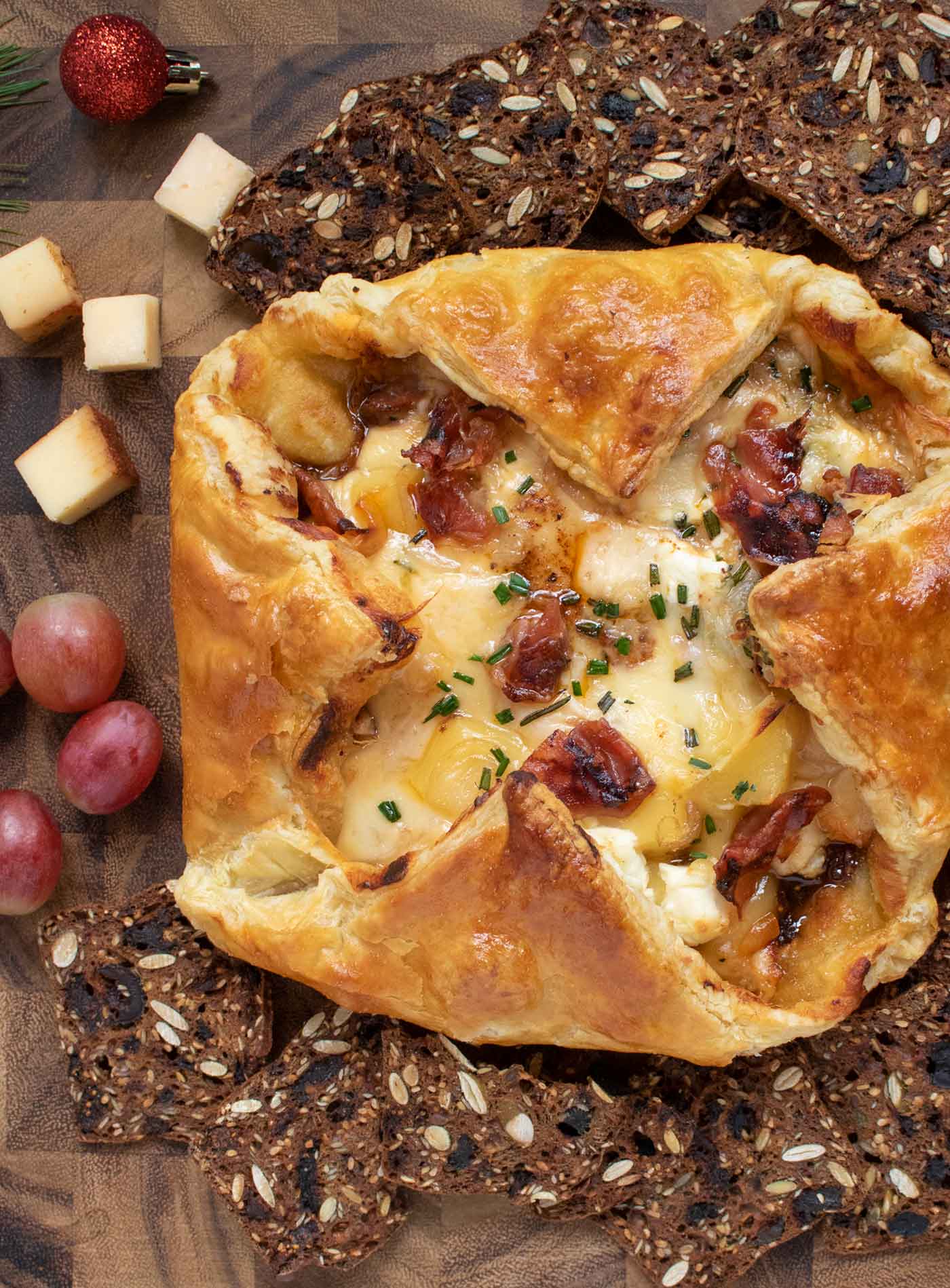 Overhead shot of Baked Cheesy Puff Pastry with Crispy Prosciutto on a serving board with crackers and fruit.