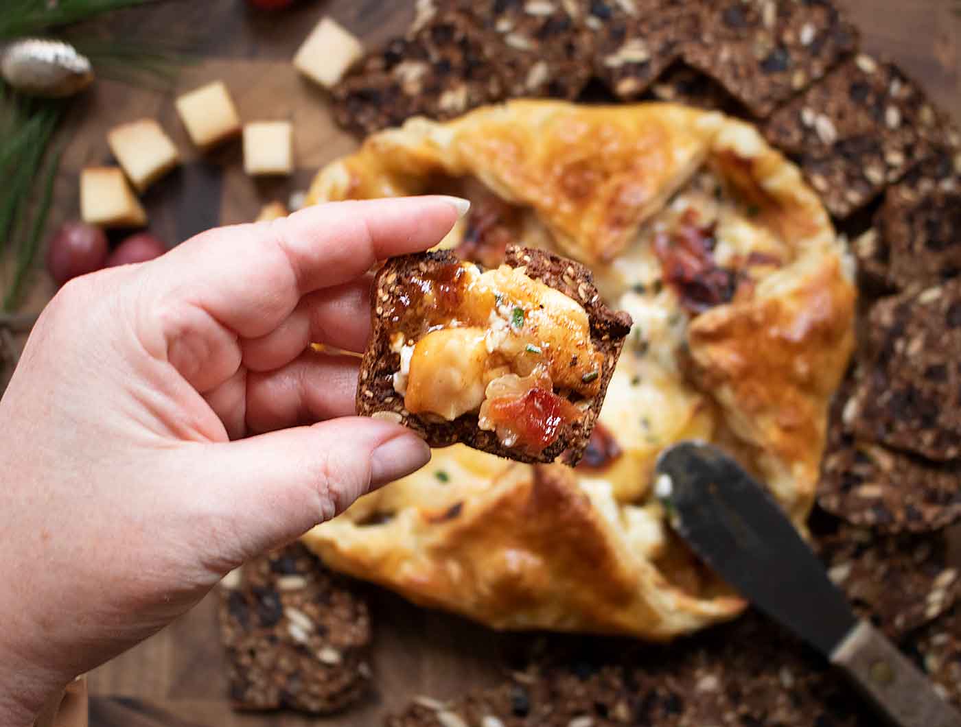 Close-up of a hand holding a cracker spread with Baked Cheesy Puff Pastry.