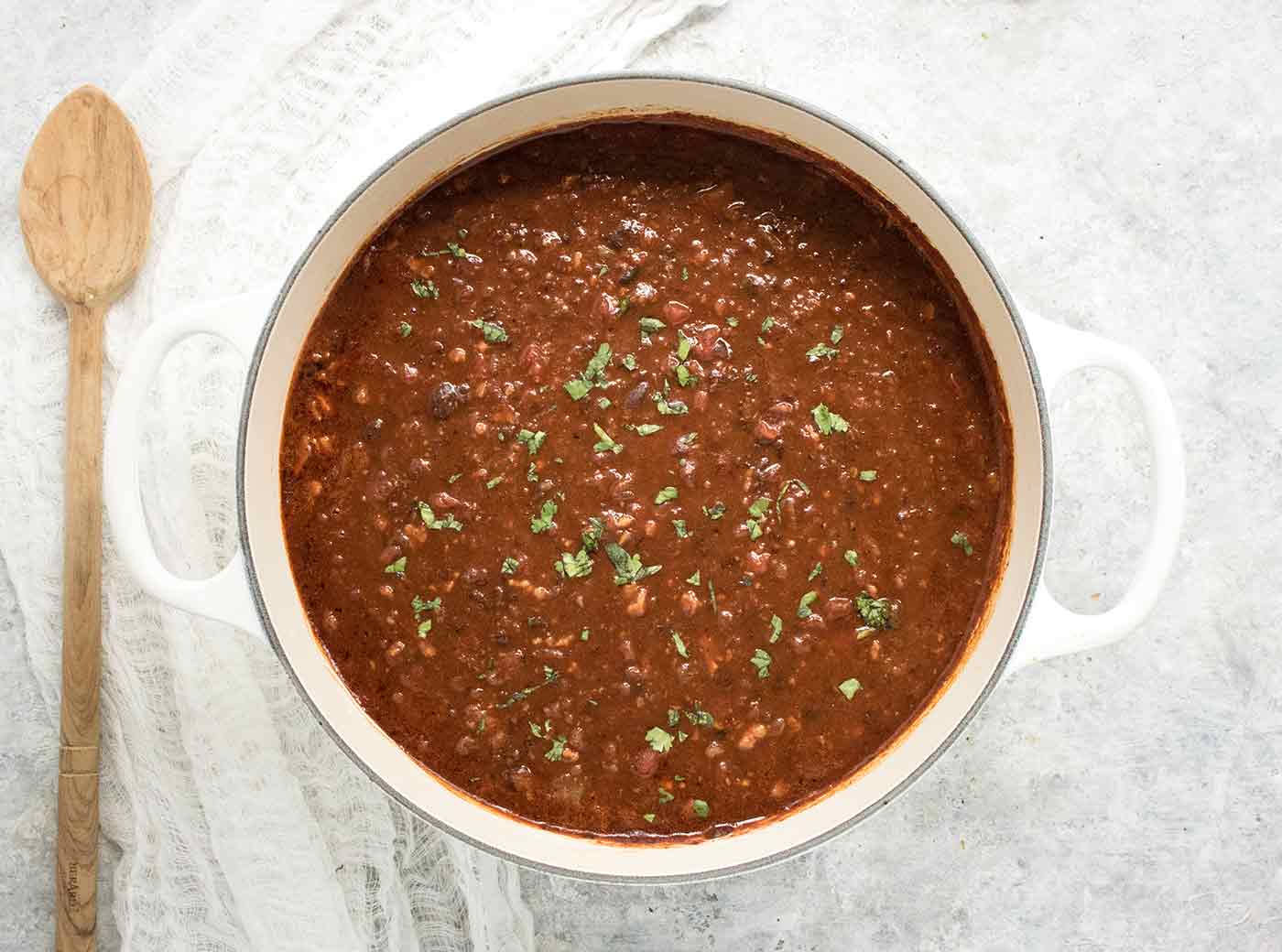 BBQ Black Bean Soup in a large white Dutch oven, next to a wooden spoon