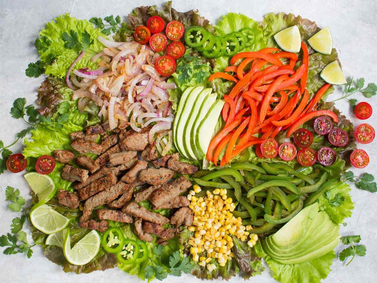 Ingredients for beef fajita salad spread out on a board.
