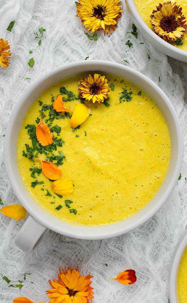 A Yellow Gazpacho in a white bowl topped with edible flowers.