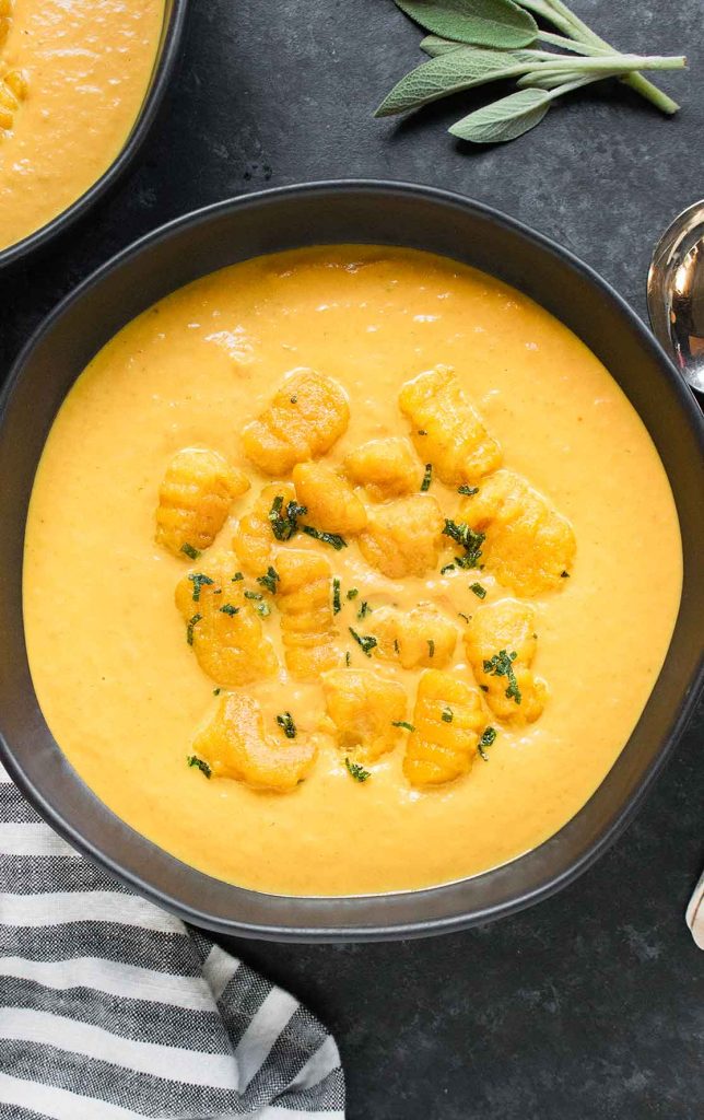 A black soup bowl filled with Creamy Pumpkin Soup and topped with Pumpkin Gnocchi.