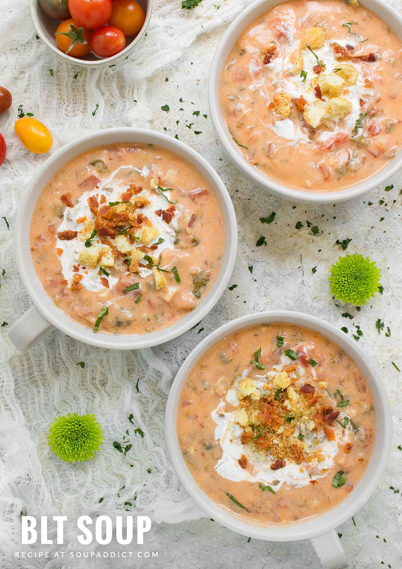 Three white mugs of BLT Soup, garnished with a swirl of creme fraiche and crushed croutons, and basil slivers