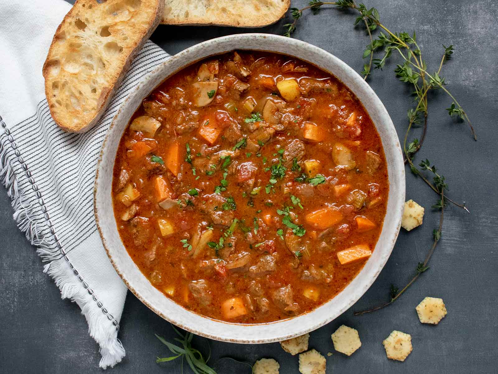 Overhead view of Braised Vegetable Beef Soup in a bowl with a side of bread and crackers.