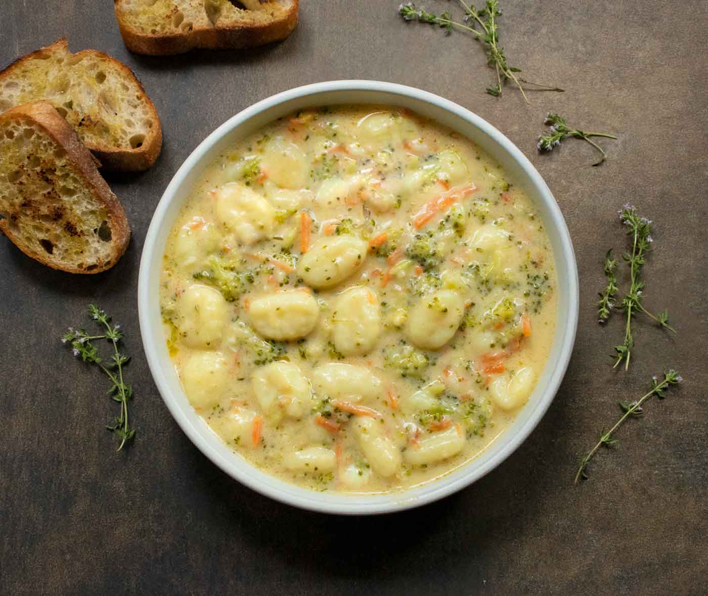 Overhead close-up view of a bowl of Broccoli Cheddar Gnocchi Soup with bread on the side.