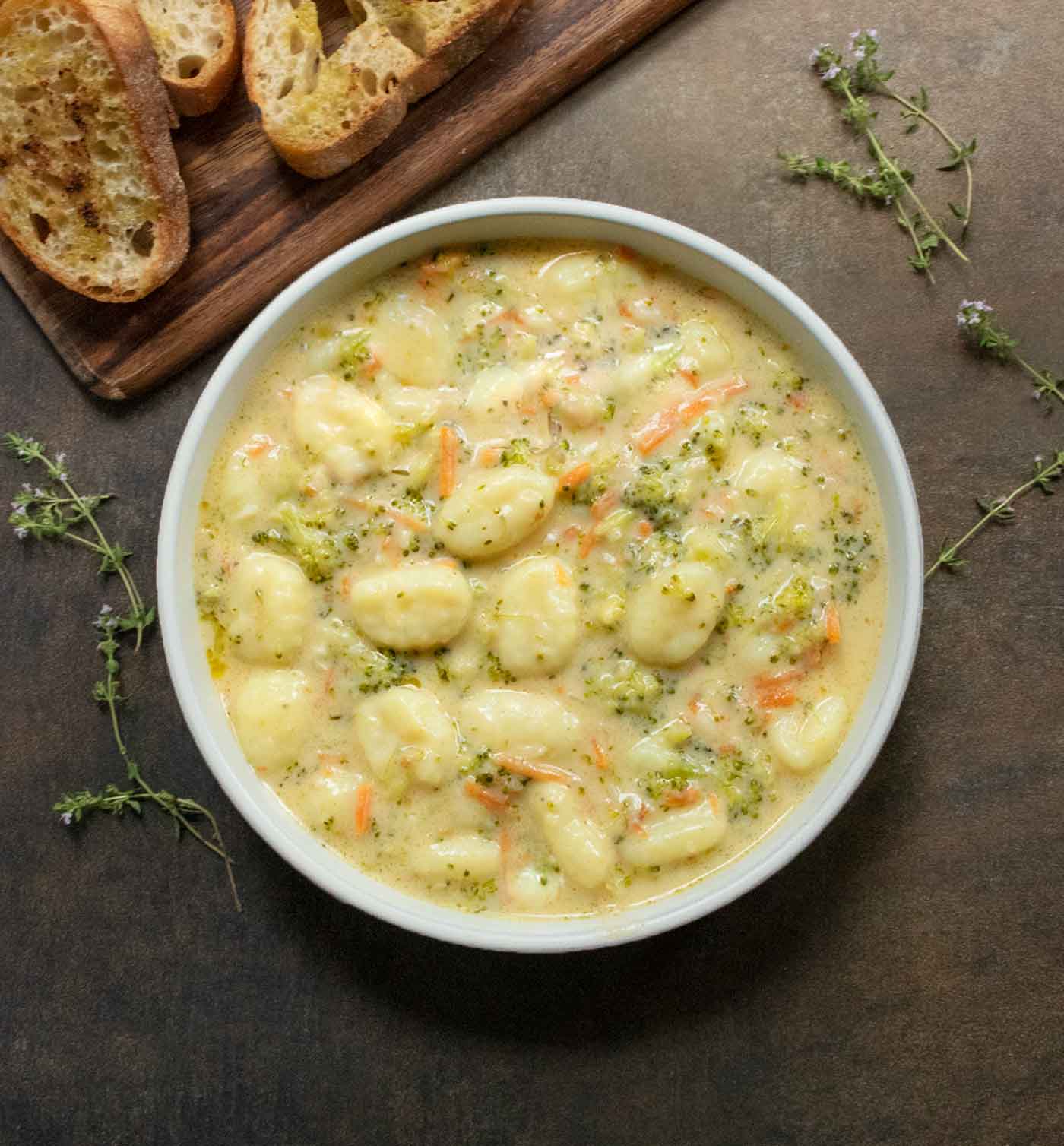 Overhead view of Broccoli Cheddar Gnocchi Soup with a side of sliced bread.