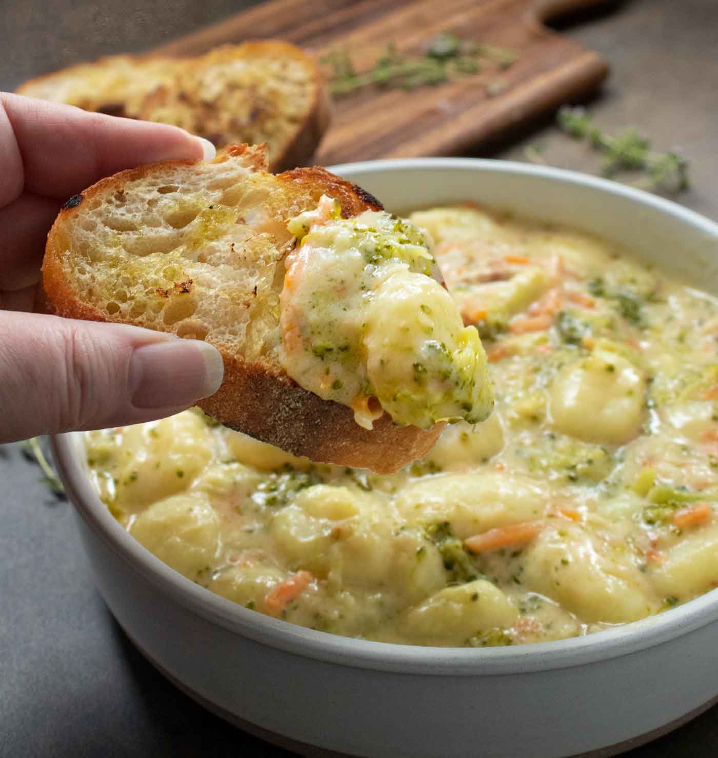 A piece of bread being dipped into the Broccoli Cheddar Gnocchi Soup.