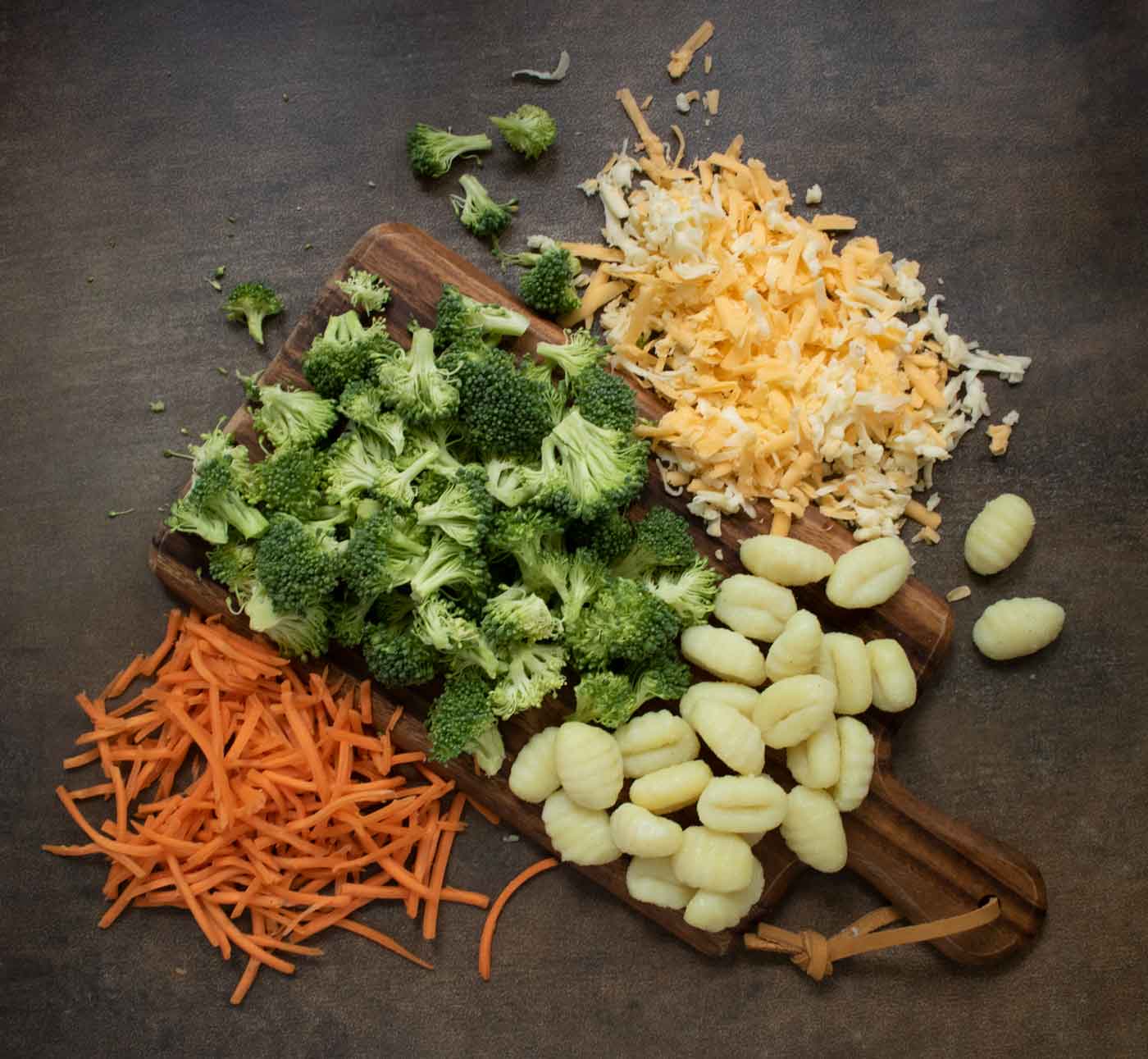 Overhead view of the main ingredients: broccoli, cheese, carrots, gnocchi, spread on a board.