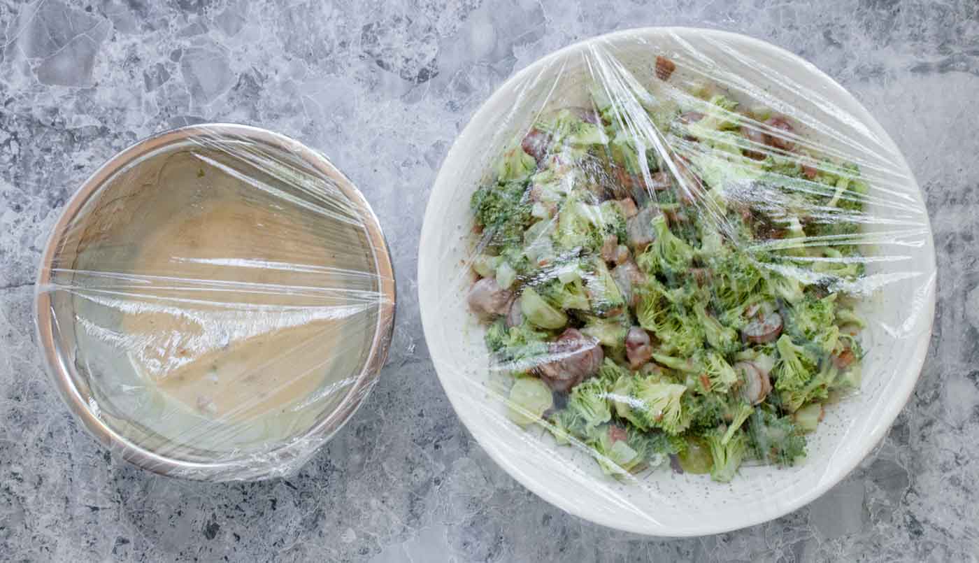 Prepping the salad and the dressing for refrigeration: bowls covered in plastic wrap.