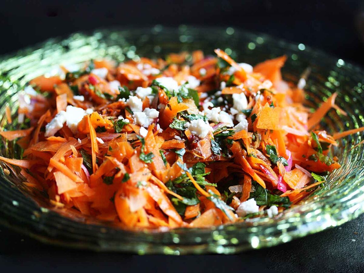 Side angled view of Carrot & Harissa Salad. in a green glass bowl.