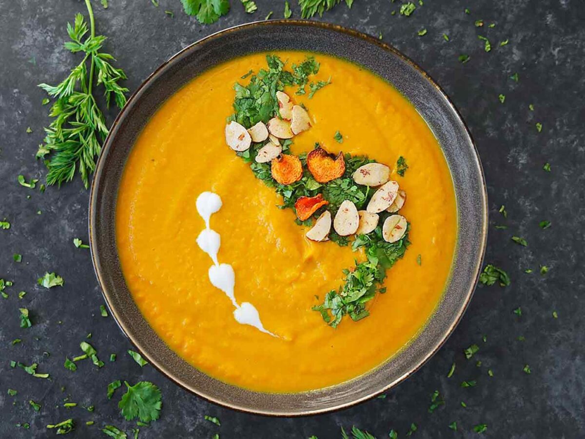 Overhead view of Carrot Turmeric Miso Soup decorated with toppings in a dark gray bowl.