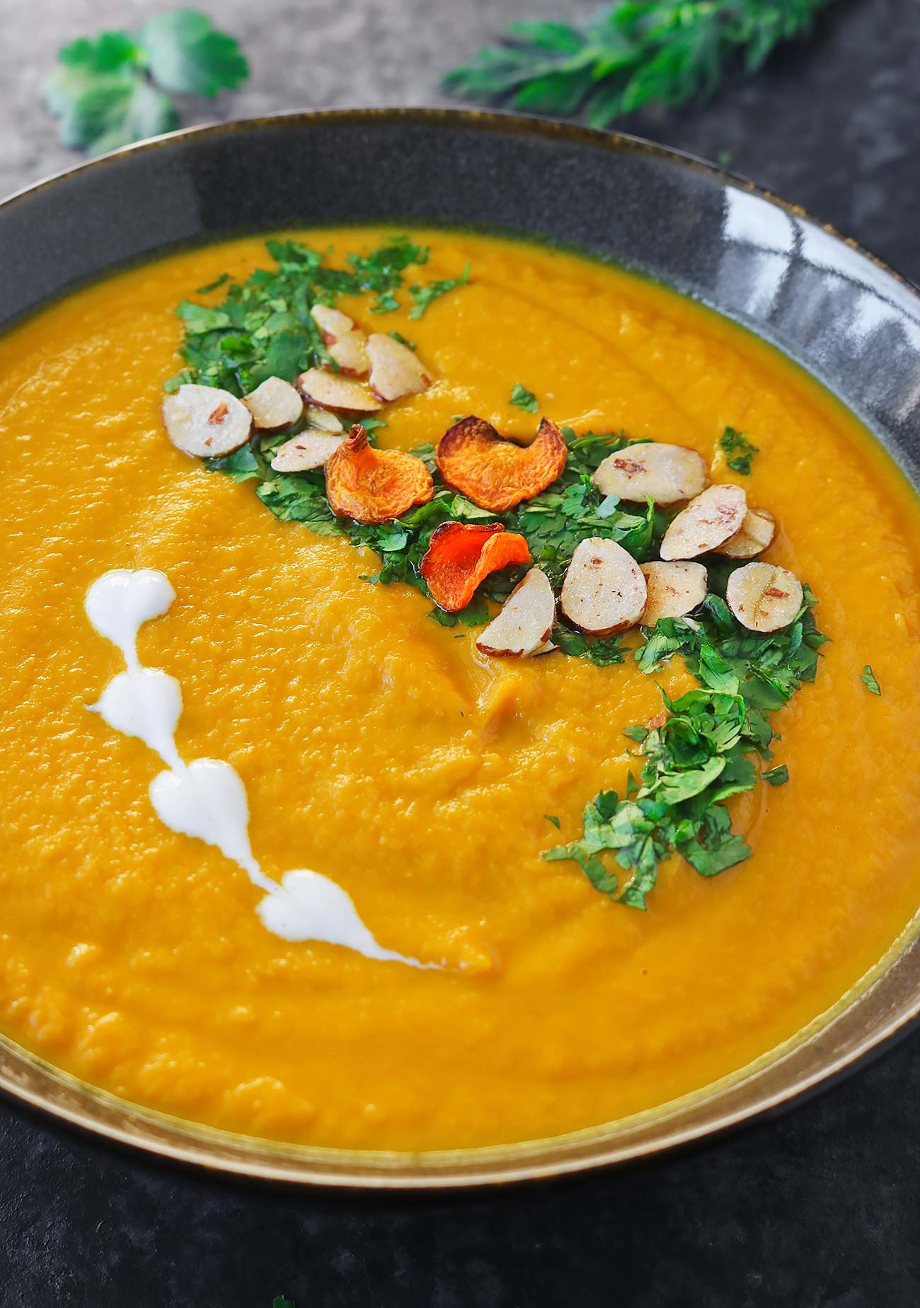 Angled view of Carrot Turmeric Miso Soup in a dark gray bowl with garnishes on top.