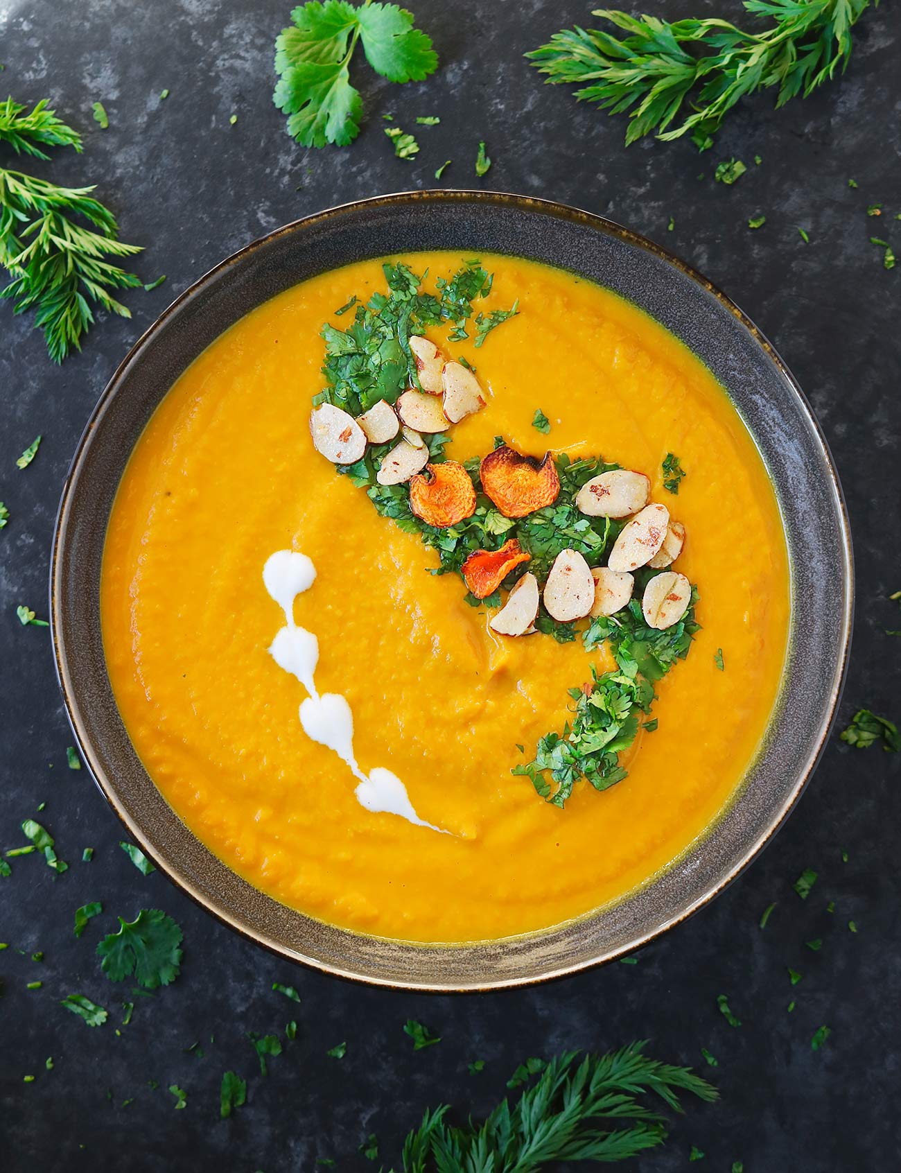 Overhead view of a bowl of Carrot Turmeric Miso with herb and almond garnishes on top.