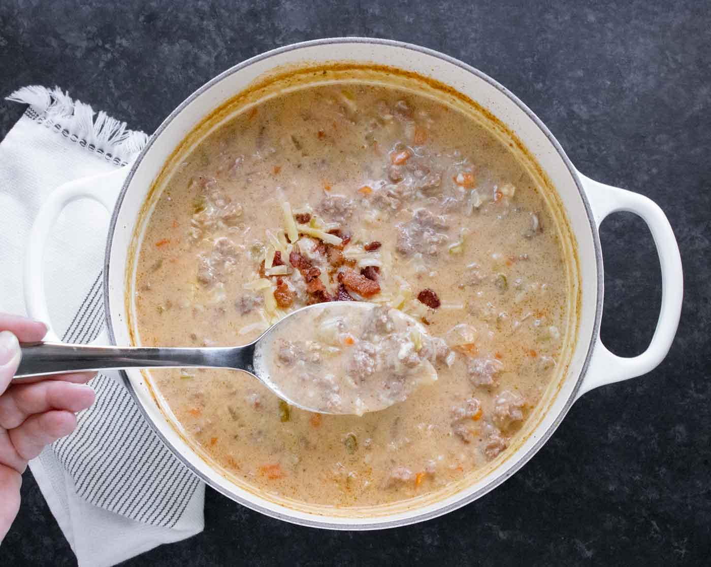 Hand holding a spoon of Cheeseburger Beer Soup out of the pot.