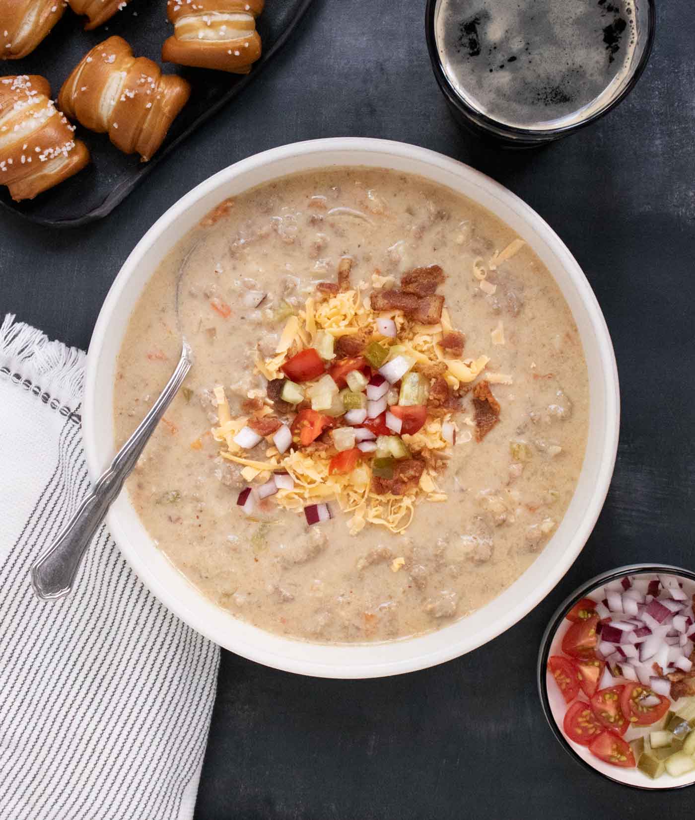 Overhead view of Cheeseburger Beer Soup in a bowl with a spoon, and pretzel bites on the side.