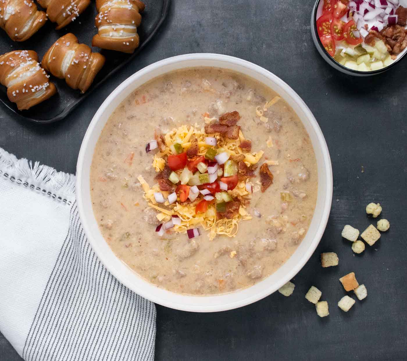 Overhead view of Cheeseburger Beer Soup in a white bowl, with soup toppings.