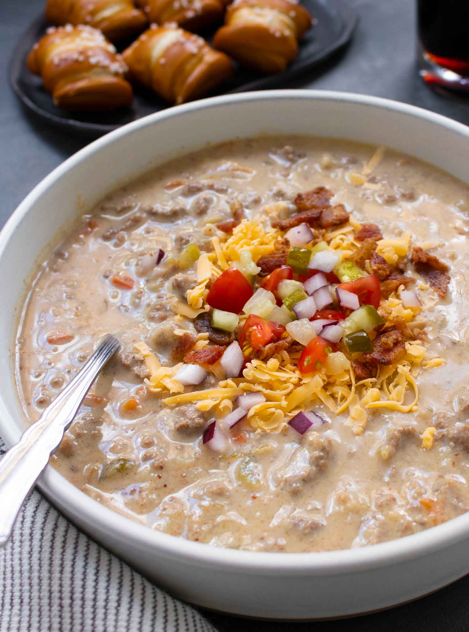 Side-angled view of a bowl of Cheeseburger Beer Soup with soup toppings.