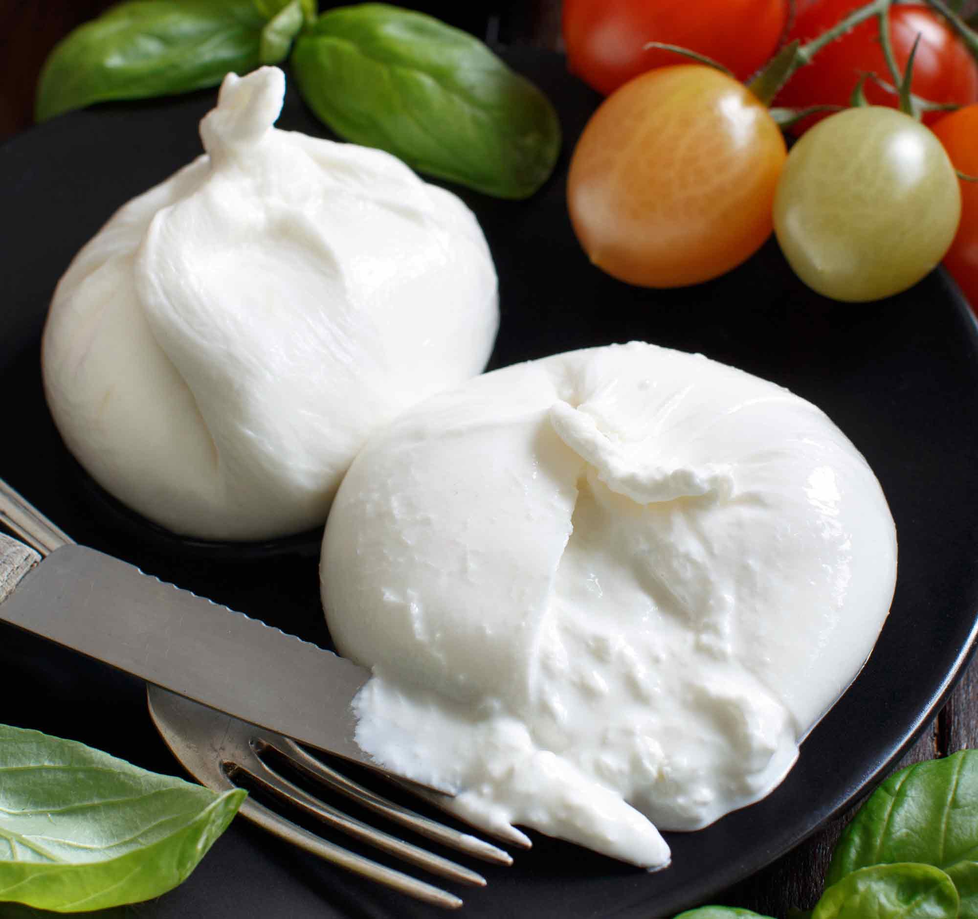 Two balls of burrata cheese on a black plate.