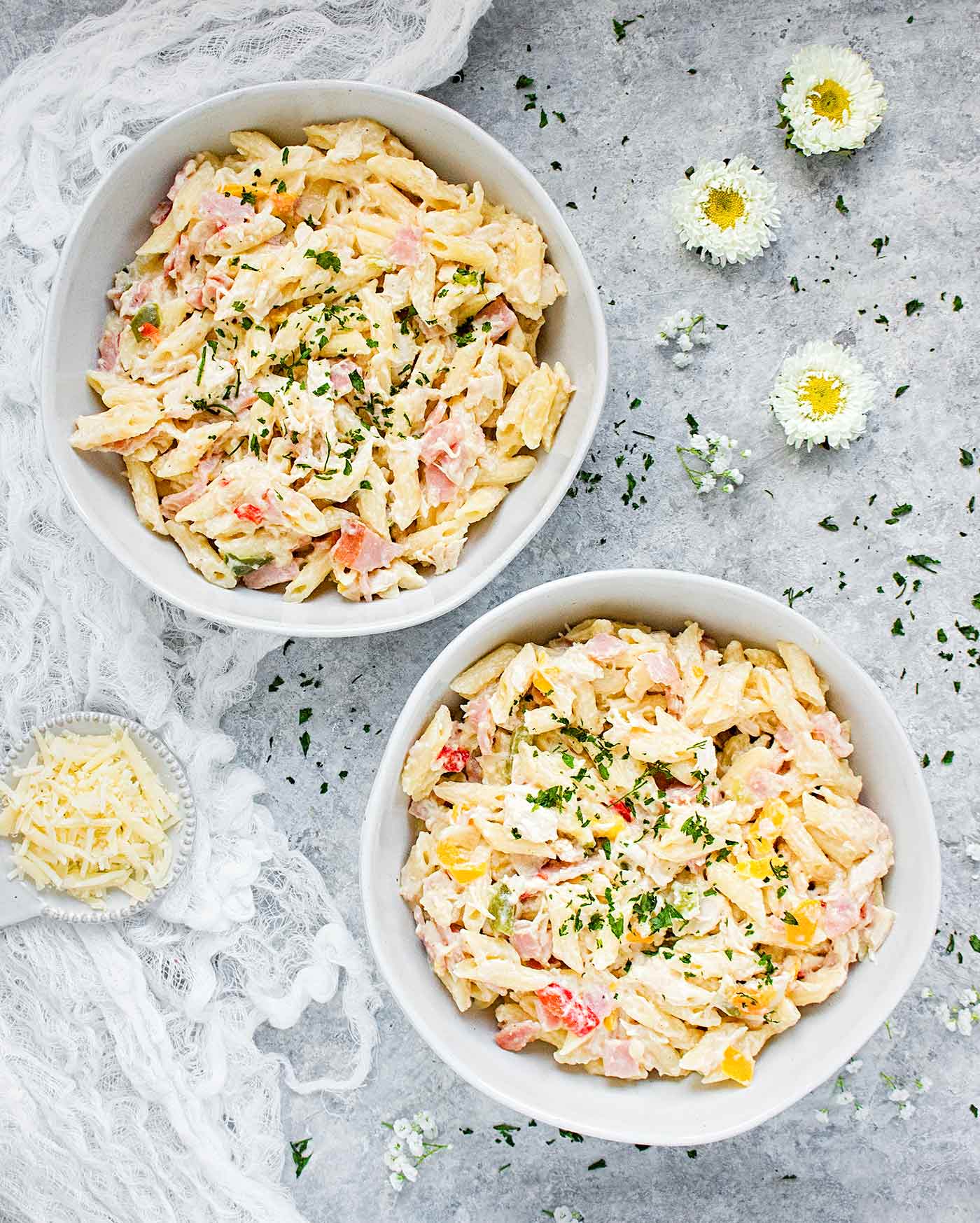 Two bowls of chicken cordon bleu pasta with parmesan cheese on the side