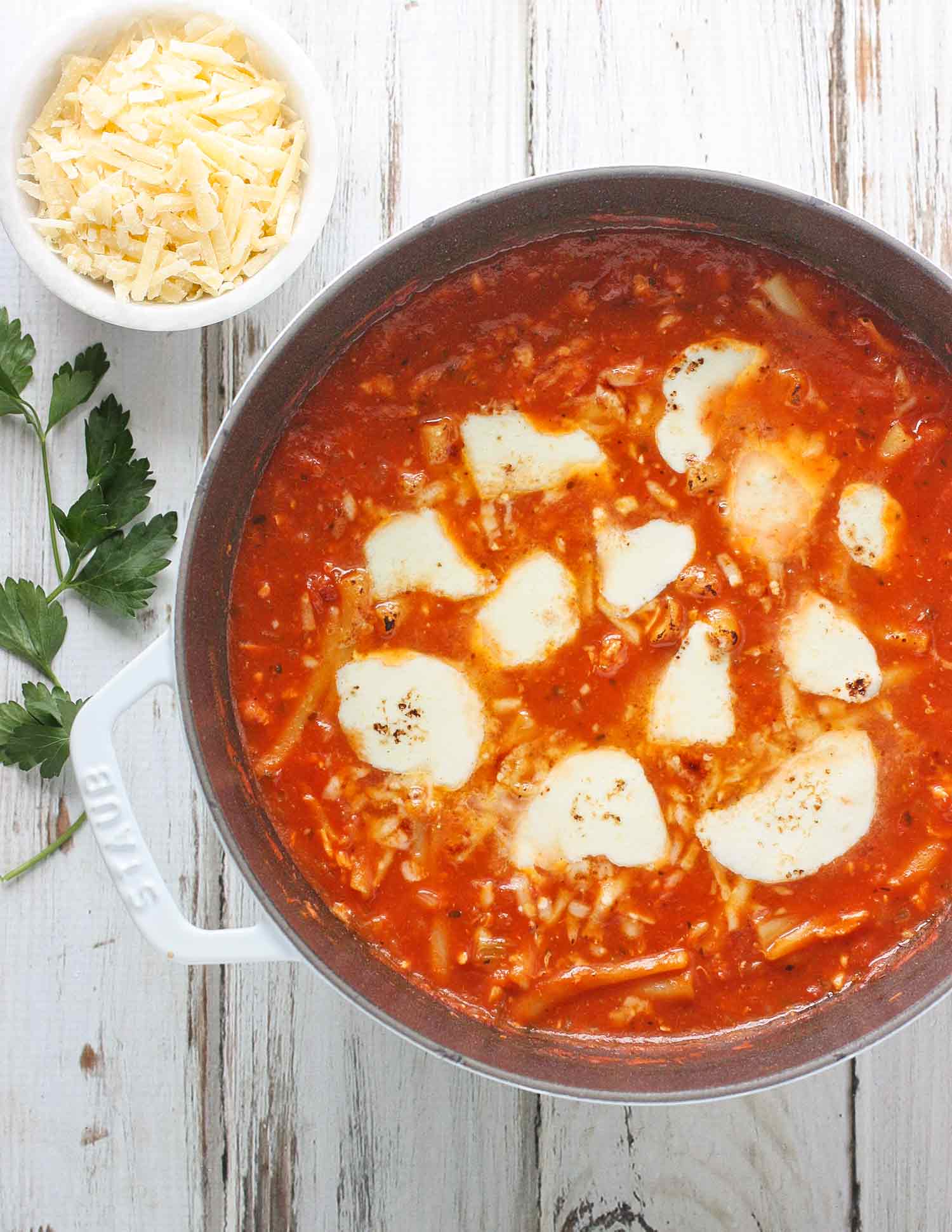 Chicken Parmesan Soup in a white Dutch oven and a side bowl of shredded parmesan cheese.