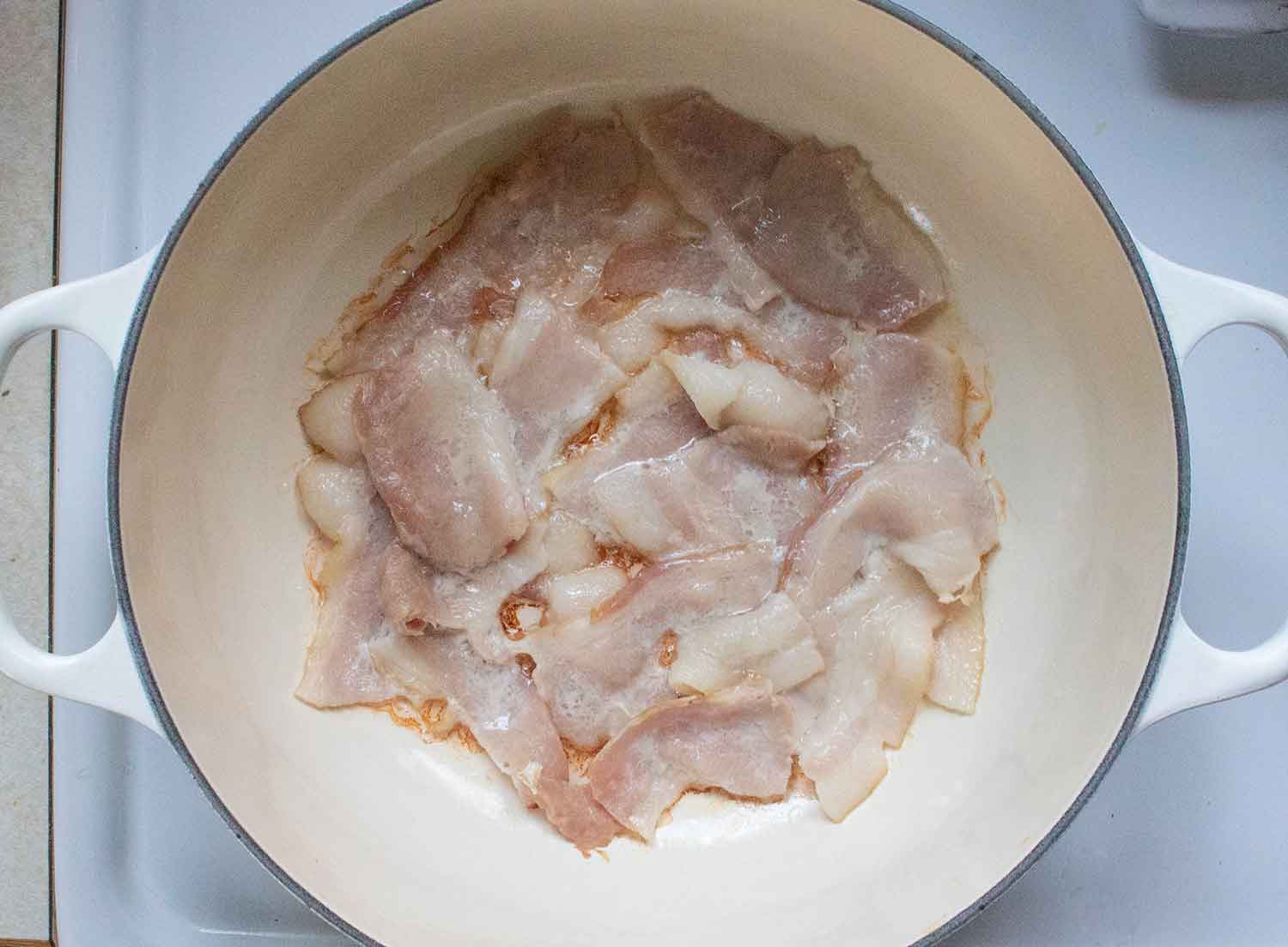 Bacon slices frying in a large Dutch oven.