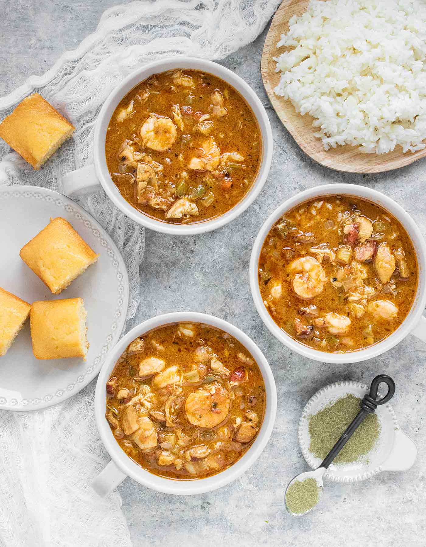 Three bowls of chicken seafood sausage gumbo, with a side of rice and cornbread, plus file powder