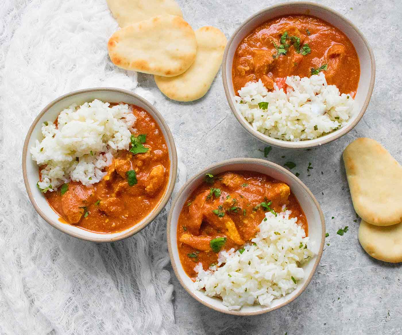 Three bowls of Chicken Tikka Masala with a side of mini naan