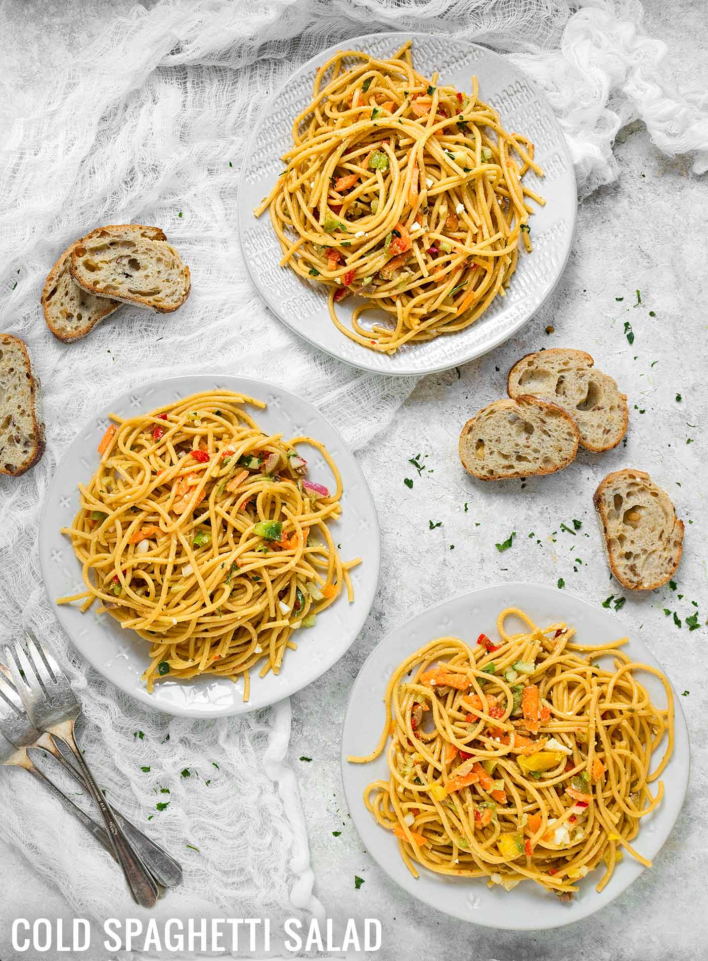 Three plates of Cold Spaghetti Salad with crusty bread on the side