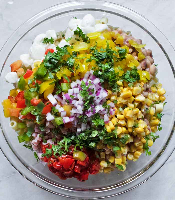 Adding the vegetables and cilantro to the base of the pasta salad.