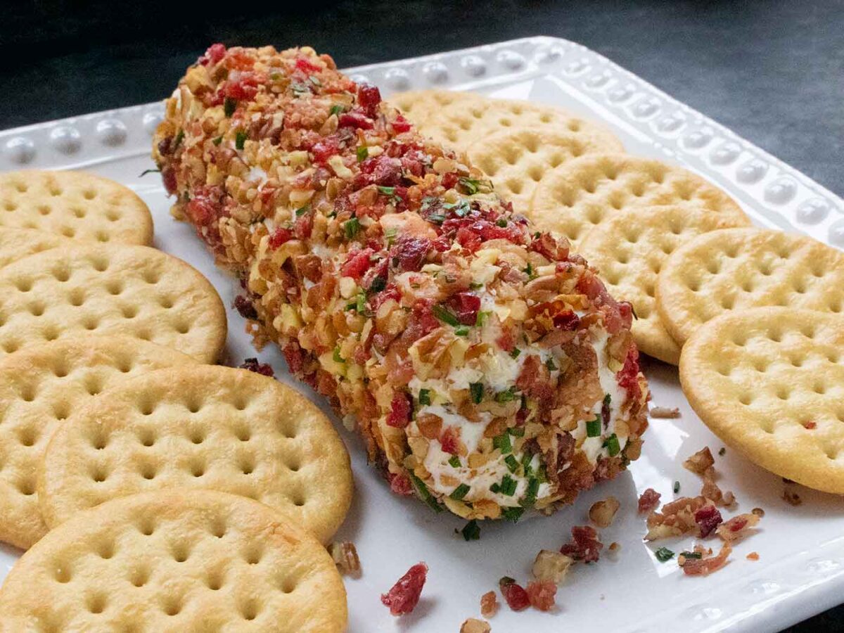 Cranberry Pecan Bacon Cheese Log on a white plate with crackers.