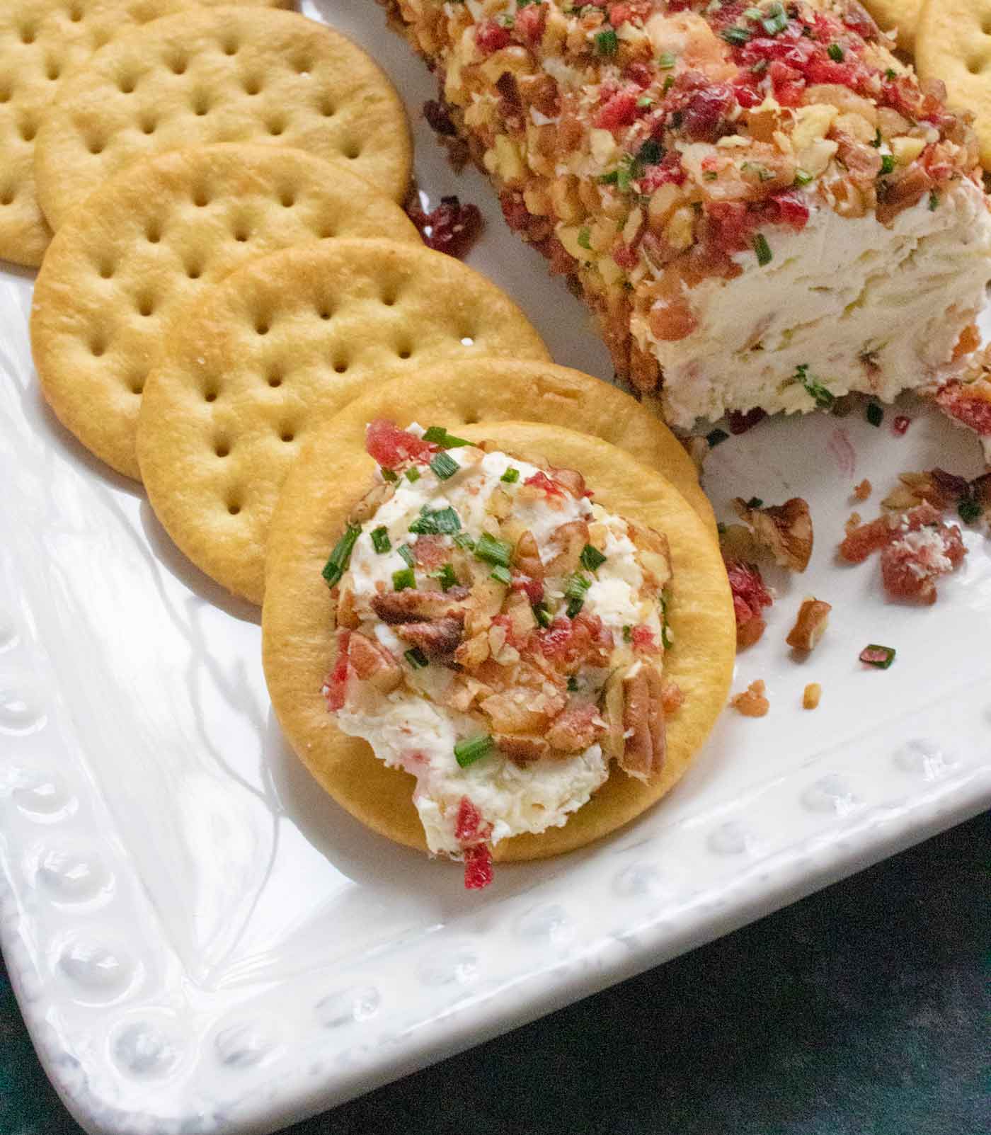 Cranberry Pecan Bacon Cheese Log with crackers, and one cracker spread with the cheese.
