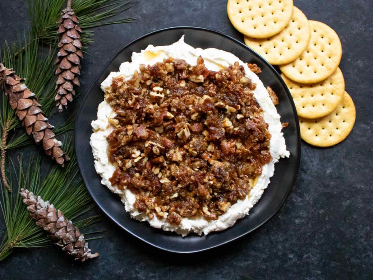 Creamy Goat Cheese Bacon Date Dip on a black plate with crackers.