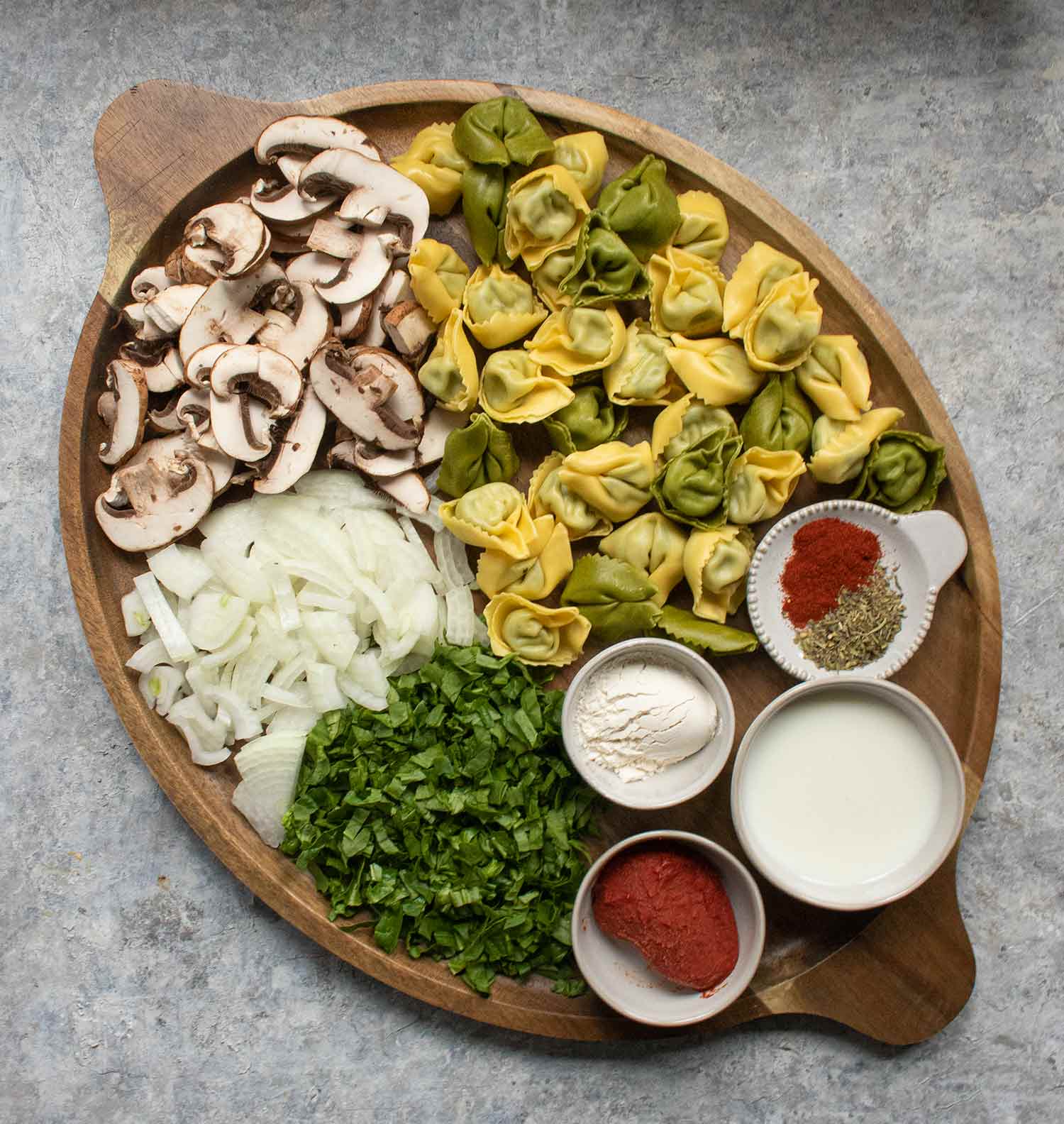 The ingredients for Creamy Mushroom Tortellini Soup arranged on a wooden serving platter.