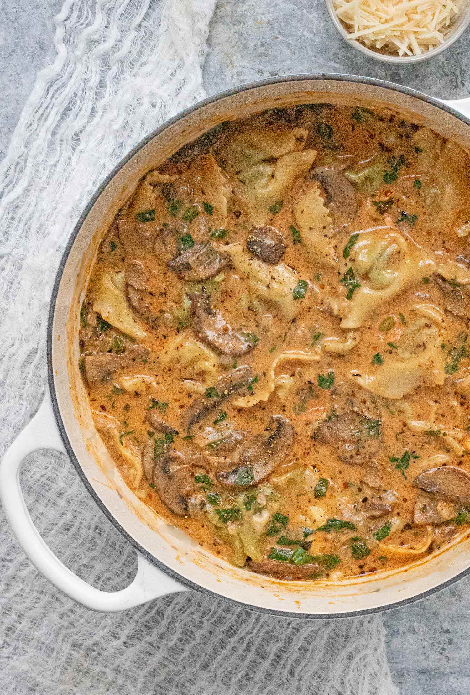 Creamy Mushroom Tortellini Soup in a white Dutch oven with a side of parmesan cheese in a bowl.