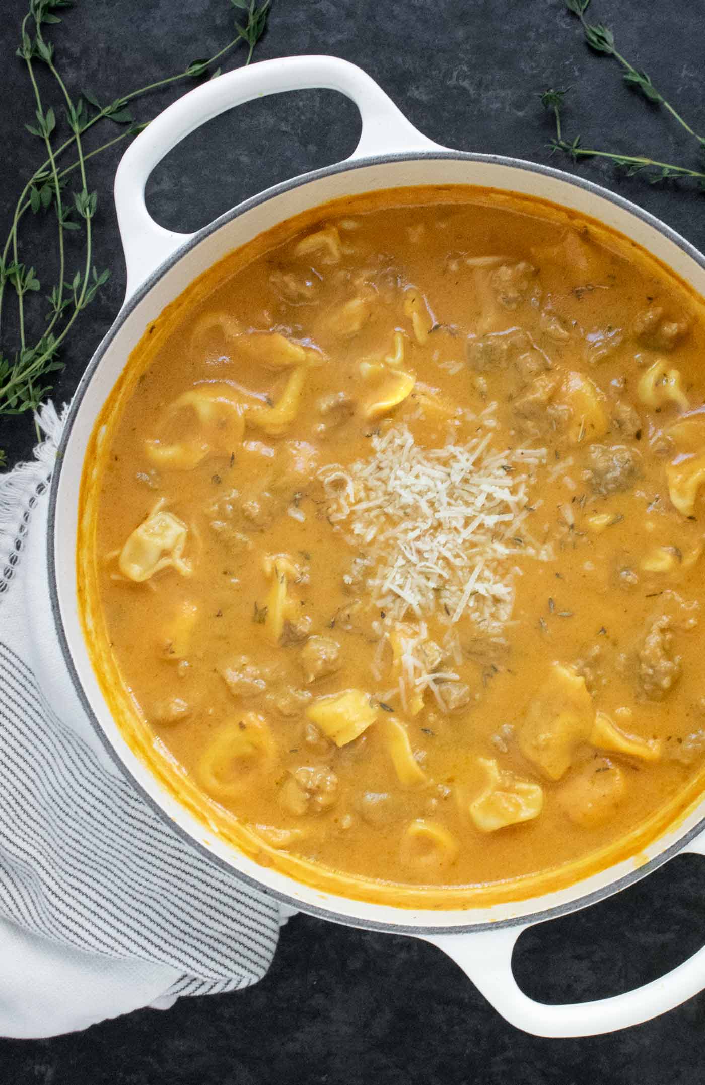 An overhead view of Creamy Pumpkin Sausage Tortellini Soup in a large white Dutch oven.
