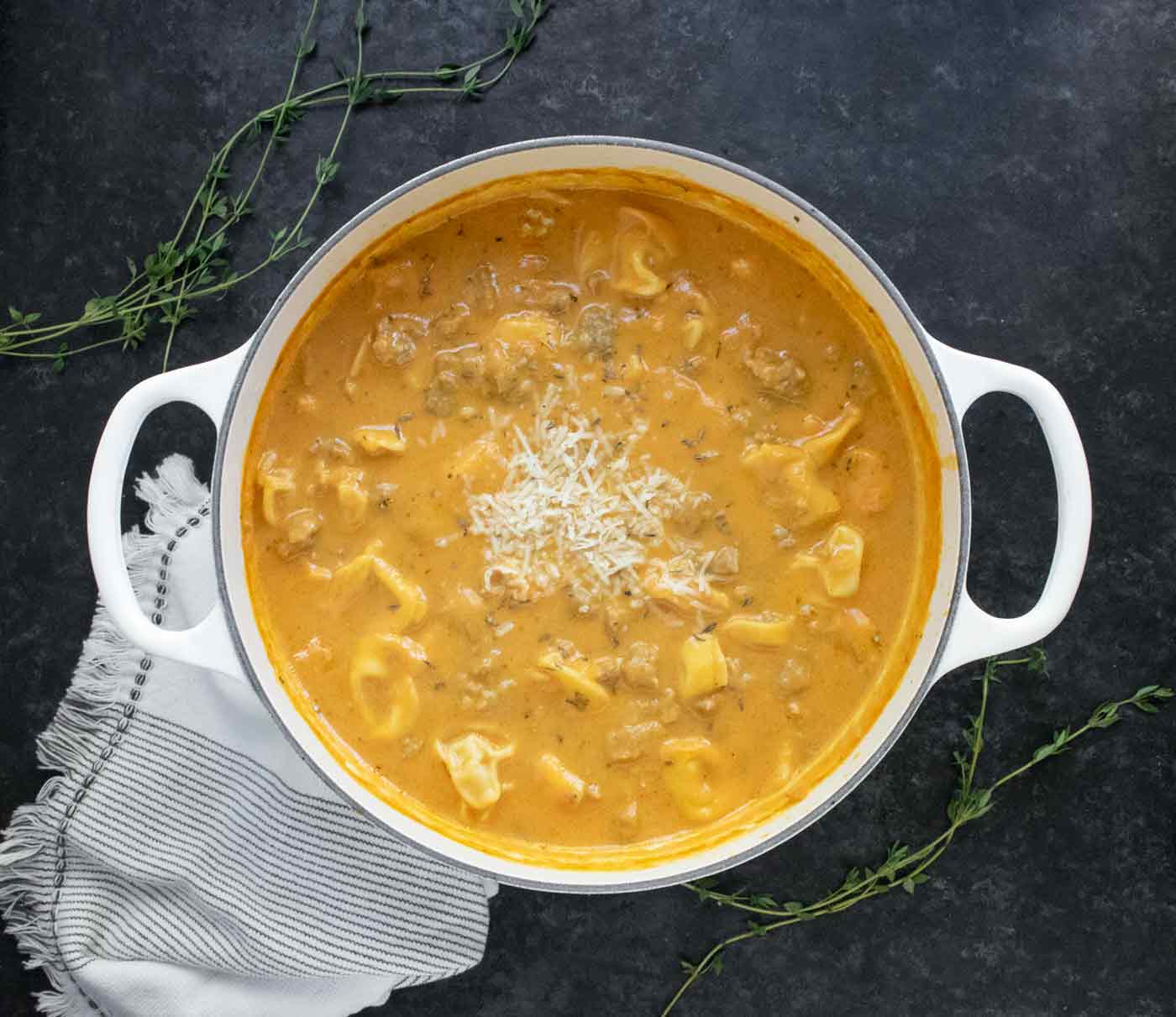Overhead view of Creamy Pumpkin Sausage Tortellini Soup in a large white Dutch oven.