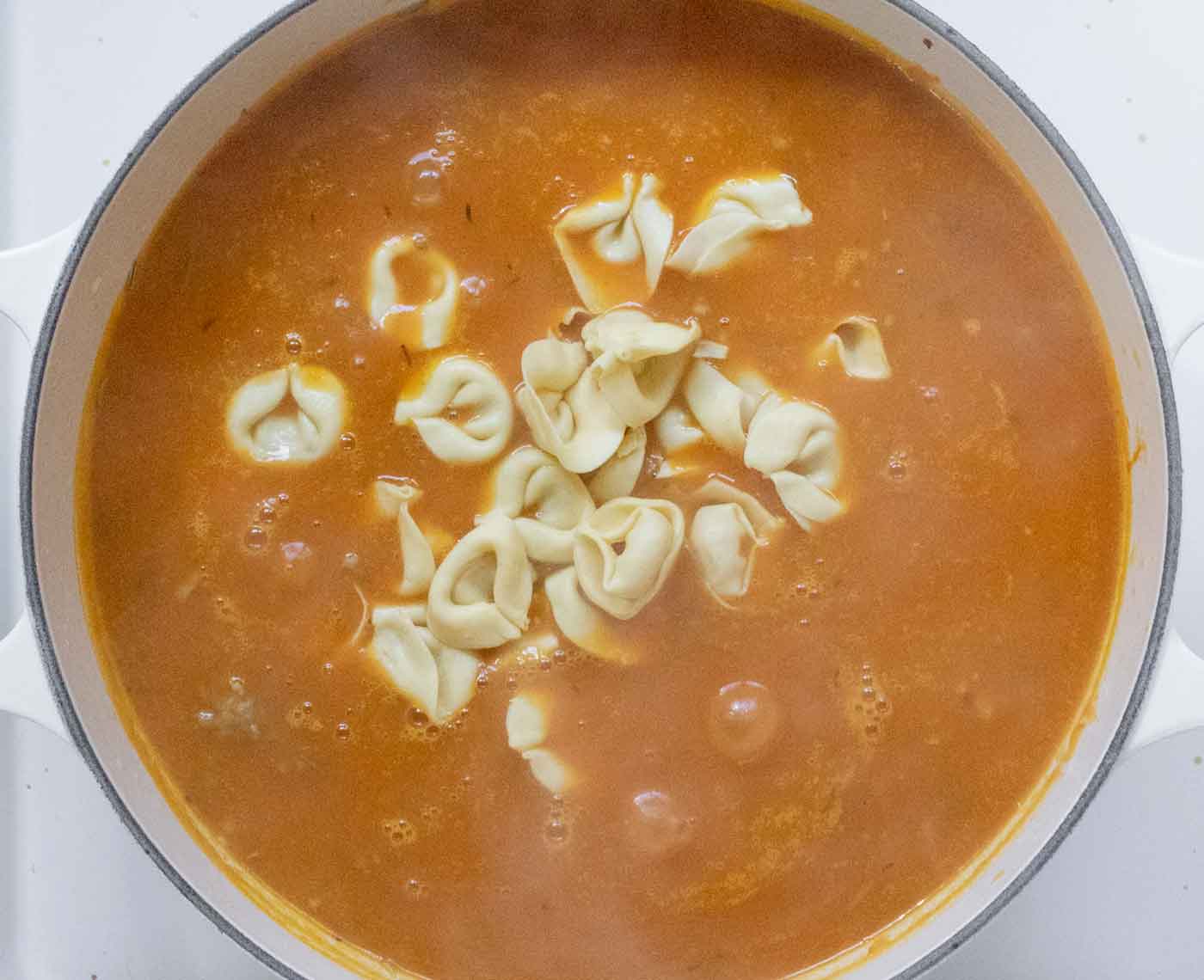 Adding the tortellini to the bubbling soup broth.