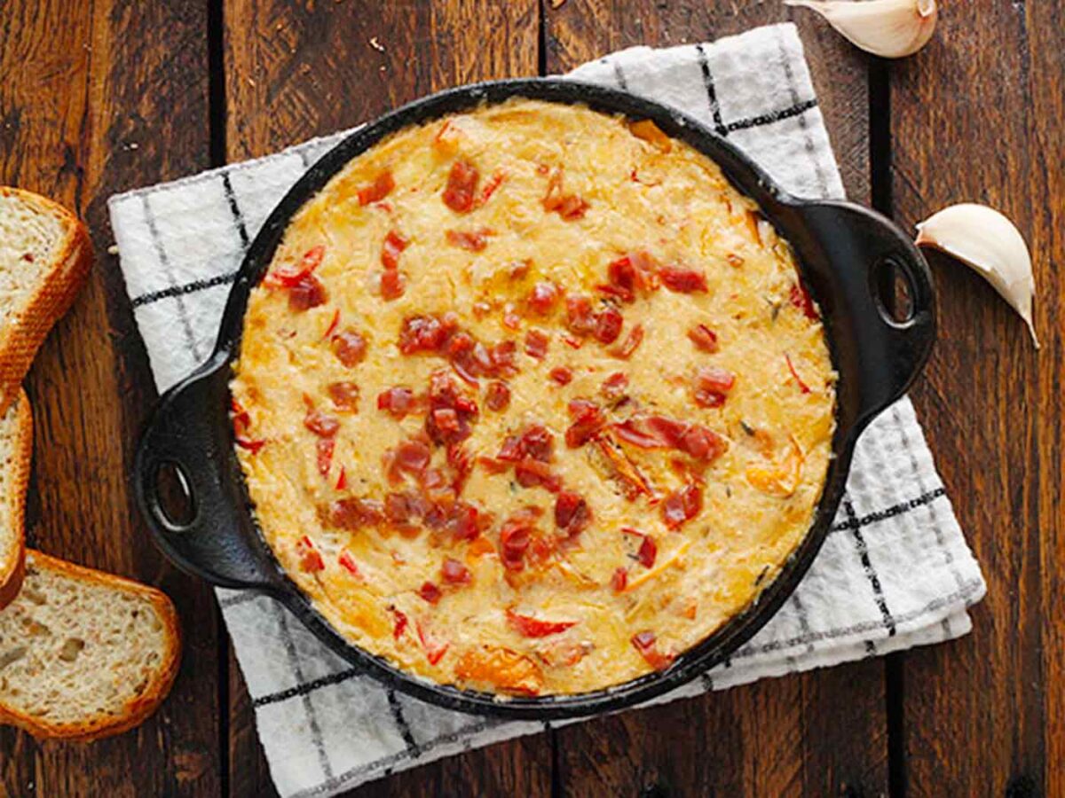 Creamy Roasted Red Pepper Dip in a black dish with crusty bread on the side.