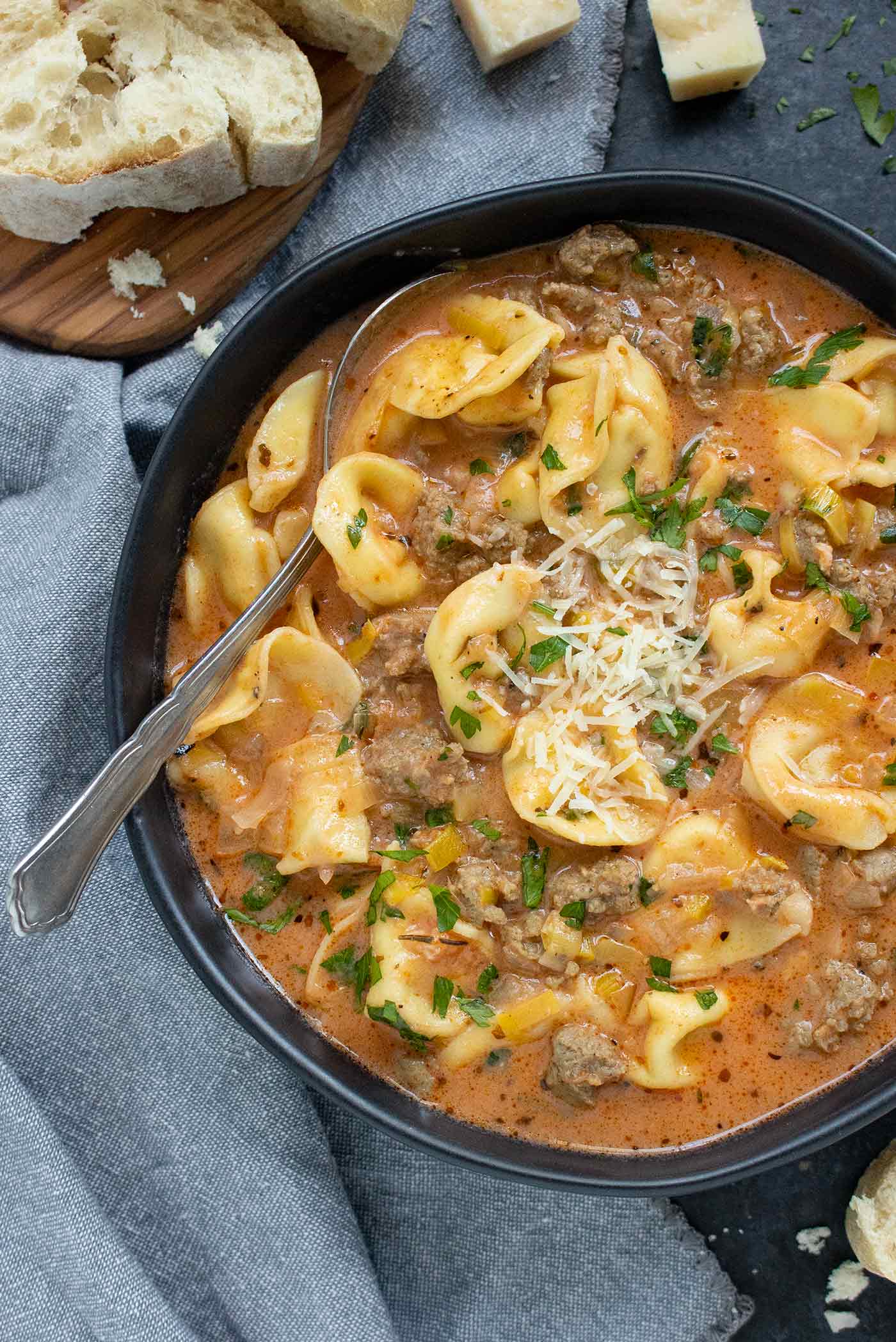 Creamy Tortellini Soup in a black bowl with a spoon.