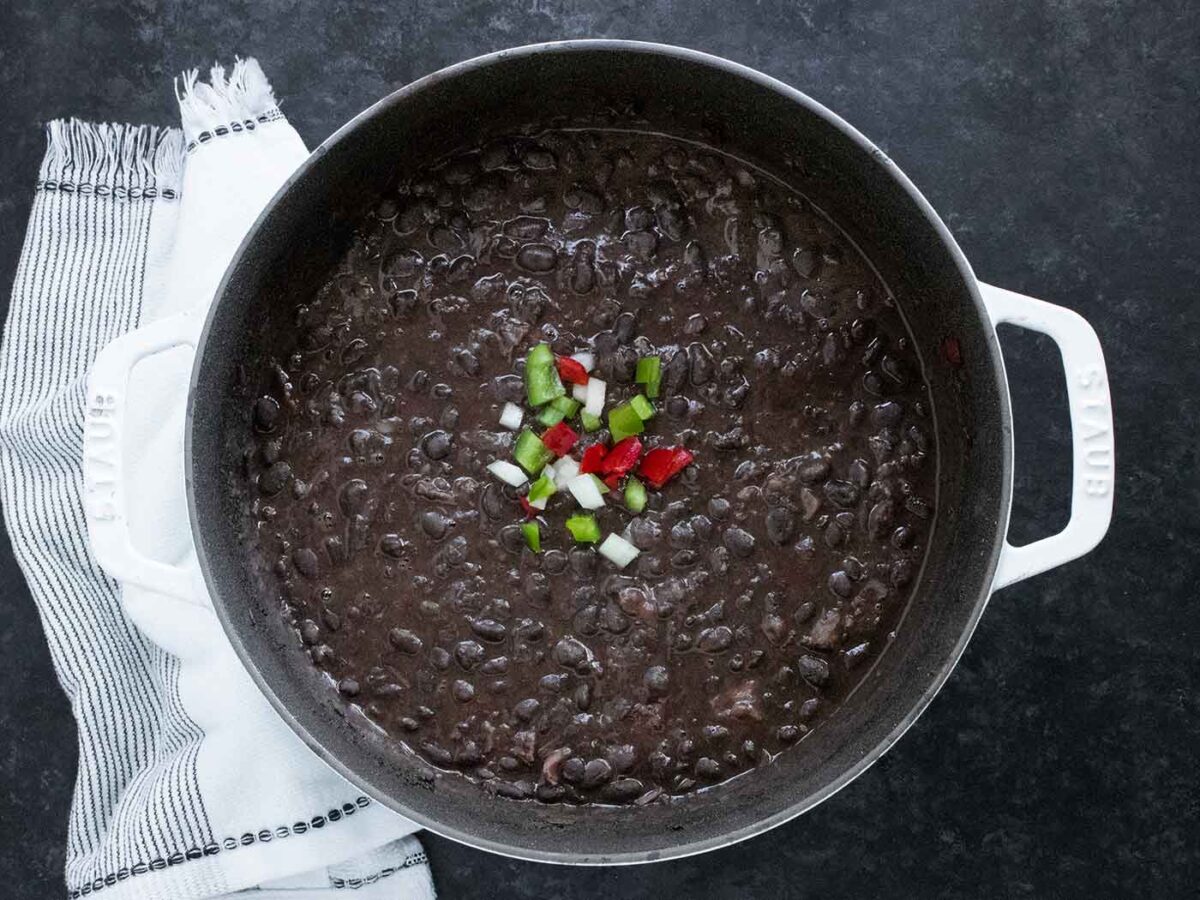 Cuban Black Bean Soup in a large white Dutch oven with a black interior, on a black background.