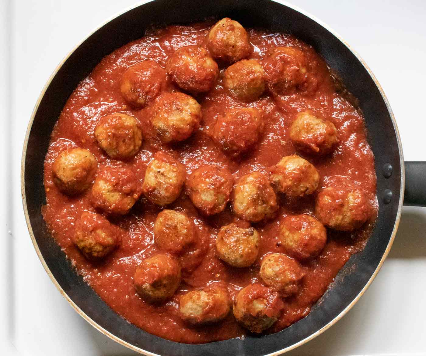 Cooked meatballs in a skillet with pizza sauce.